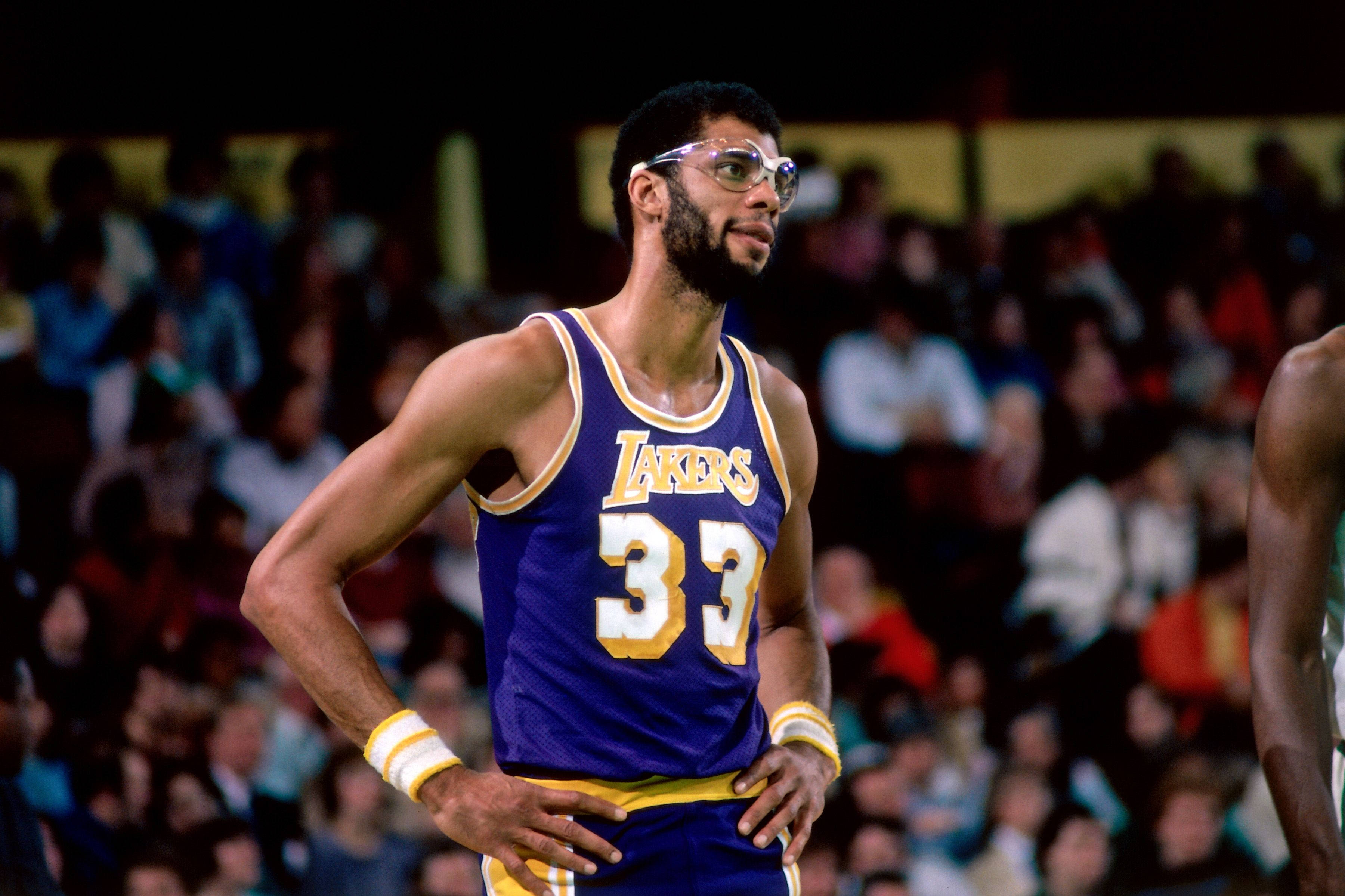 Kareem 桌布 壁紙 — 一位專注的籃球運動員穿著紫色湖人隊33號球衣，在明亮的場館燈光下比賽時雙手叉腰站立。