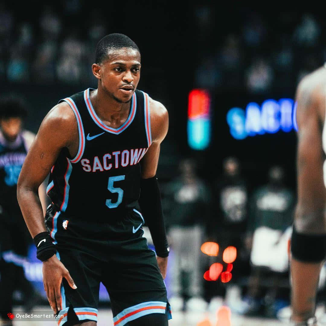 NBA 桌布 壁紙 — 一位專注的籃球運動員穿著黑色Sactown球衣，號碼5，在比賽期間準備就緒，站在燈光明亮的球場上。