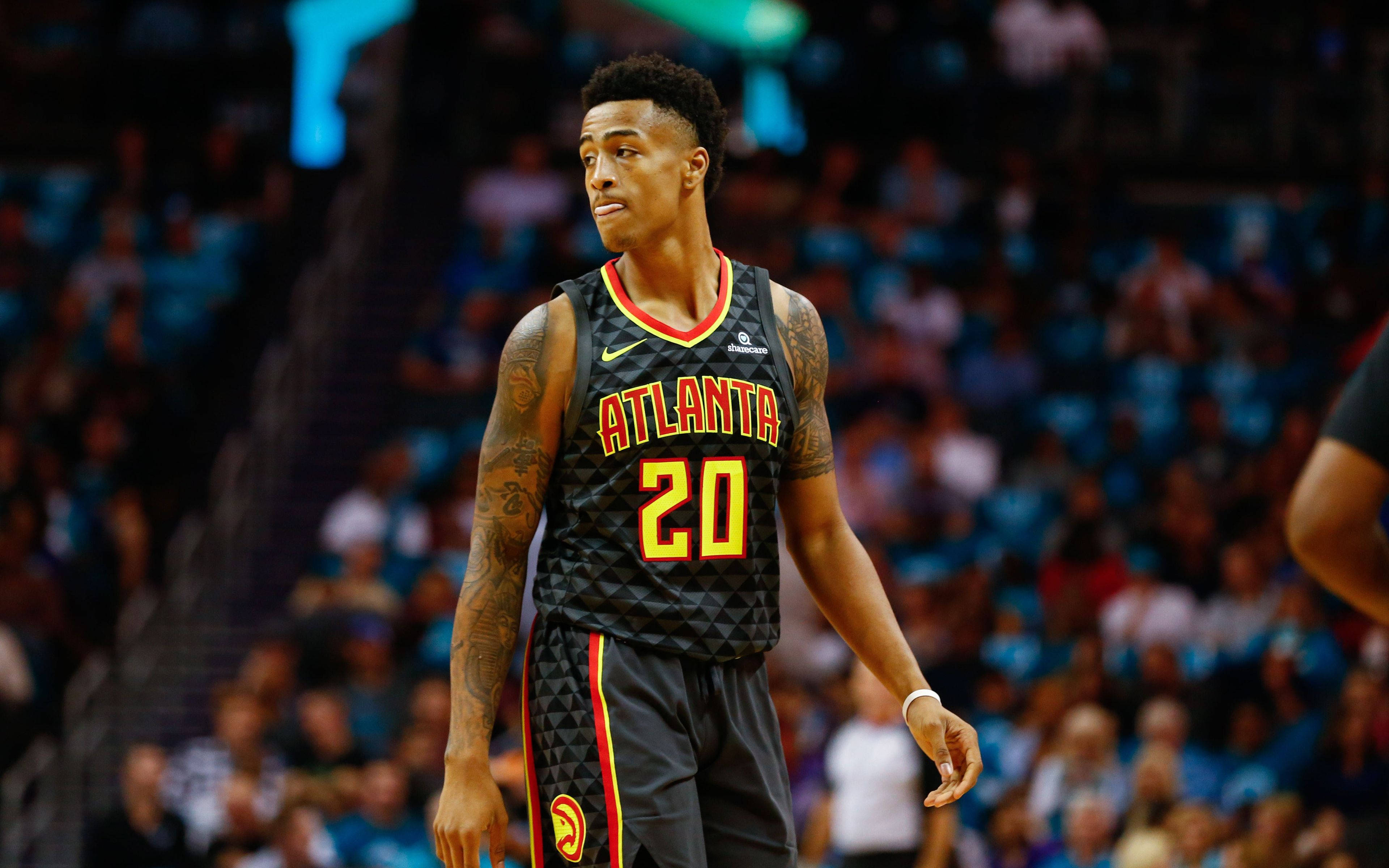 John Collins 桌布 壁紙 — 一位專注的籃球運動員身穿亞特蘭大老鷹隊球衣，站在球場上，背景是模糊的觀眾。