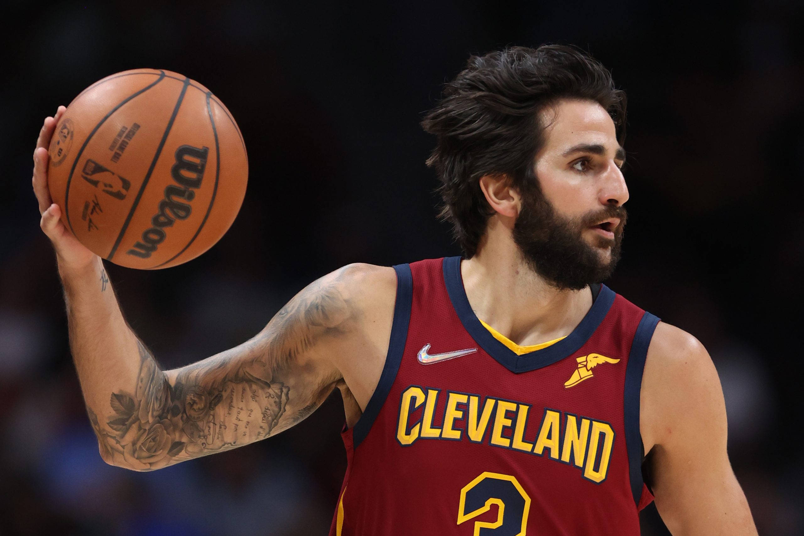 Ricky Rubio 桌布 壁紙 — 一位專注的籃球運動員身穿克里夫蘭球衣，在場館燈光下於比賽中手持威爾遜籃球。