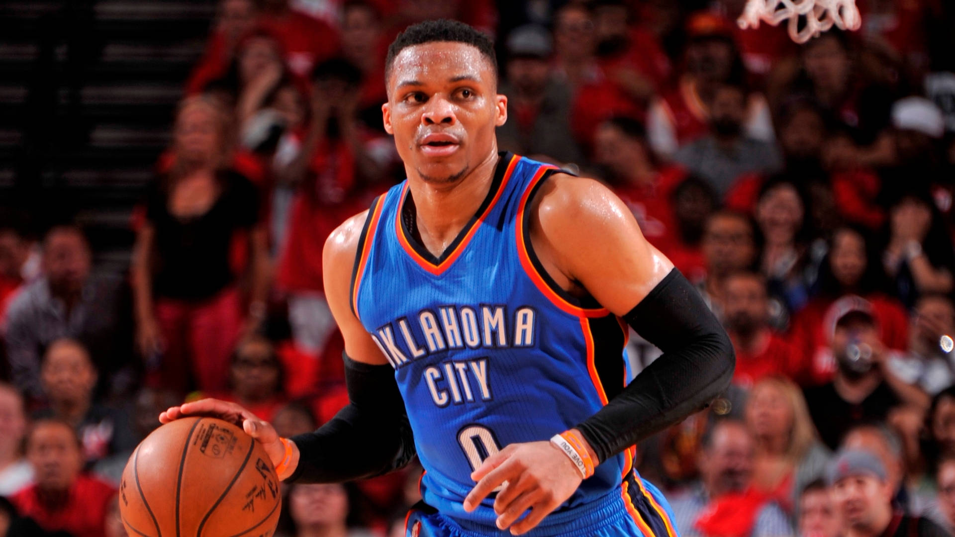 Westbrook 桌布 壁紙 — 一位專注的籃球運動員身穿奧克拉荷馬城球衣，在模糊的人群背景下運球比賽。