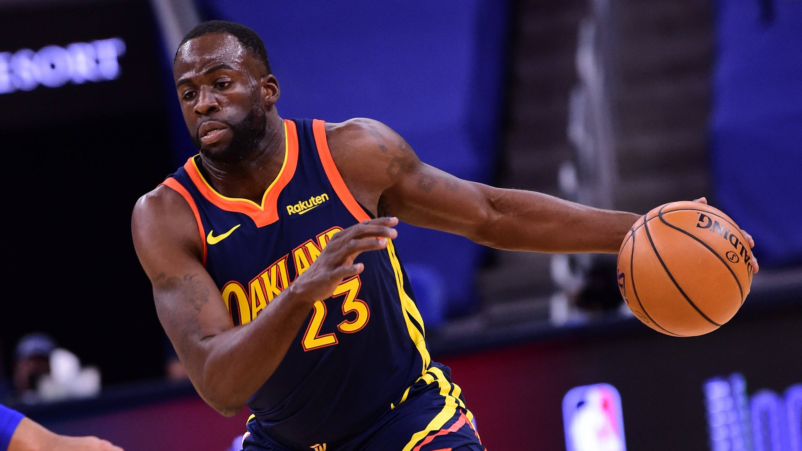 Draymond Green 桌布 壁紙 — 一位專注的籃球運動員身穿奧克蘭球衣，在明亮的場館燈光下於激烈的比賽中運球。