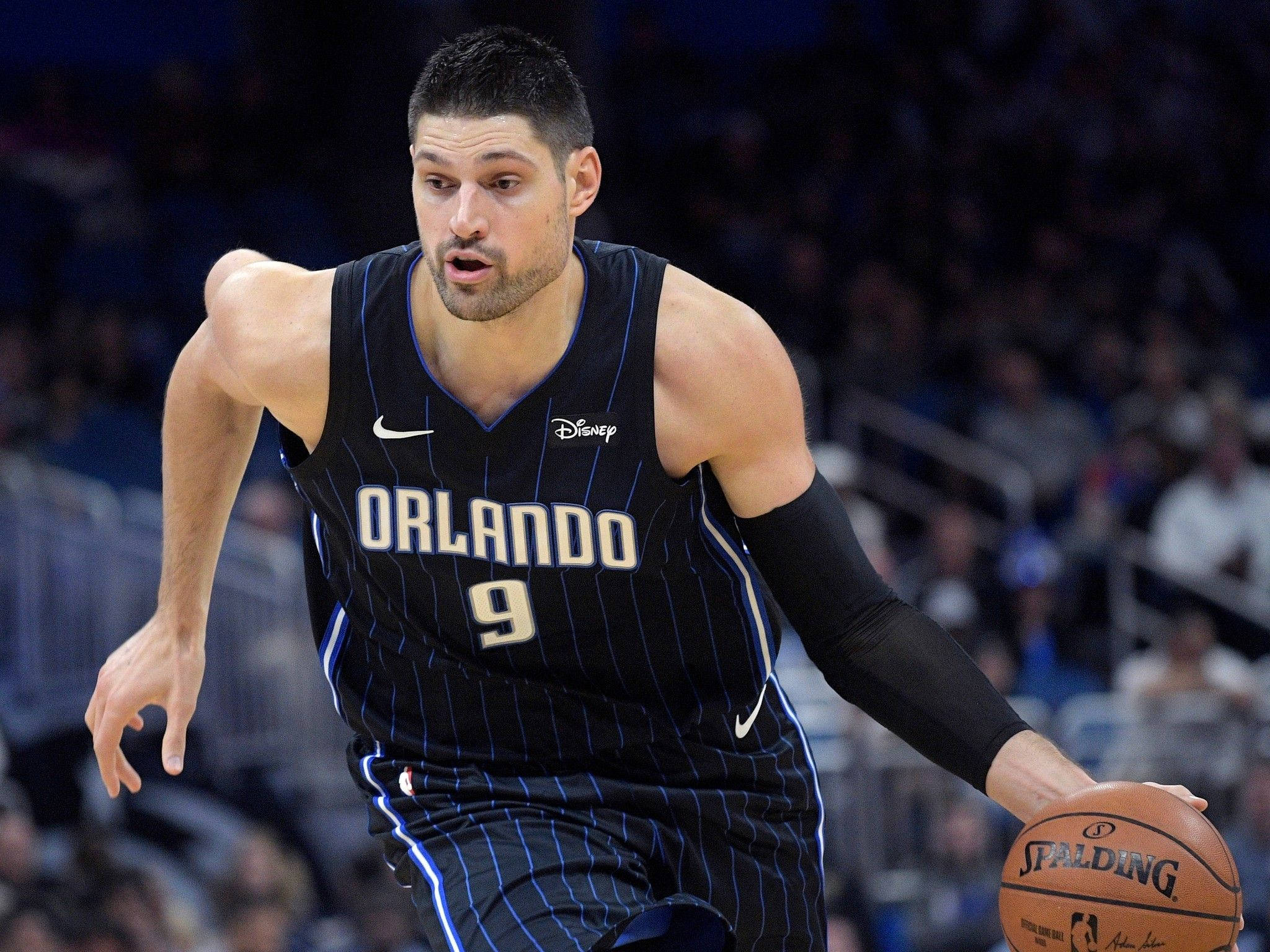 NBA 桌布 壁紙 — 一位專注的籃球運動員身穿奧蘭多魔術隊球衣，在場館燈光下進行激烈比賽時運著斯伯丁籃球。