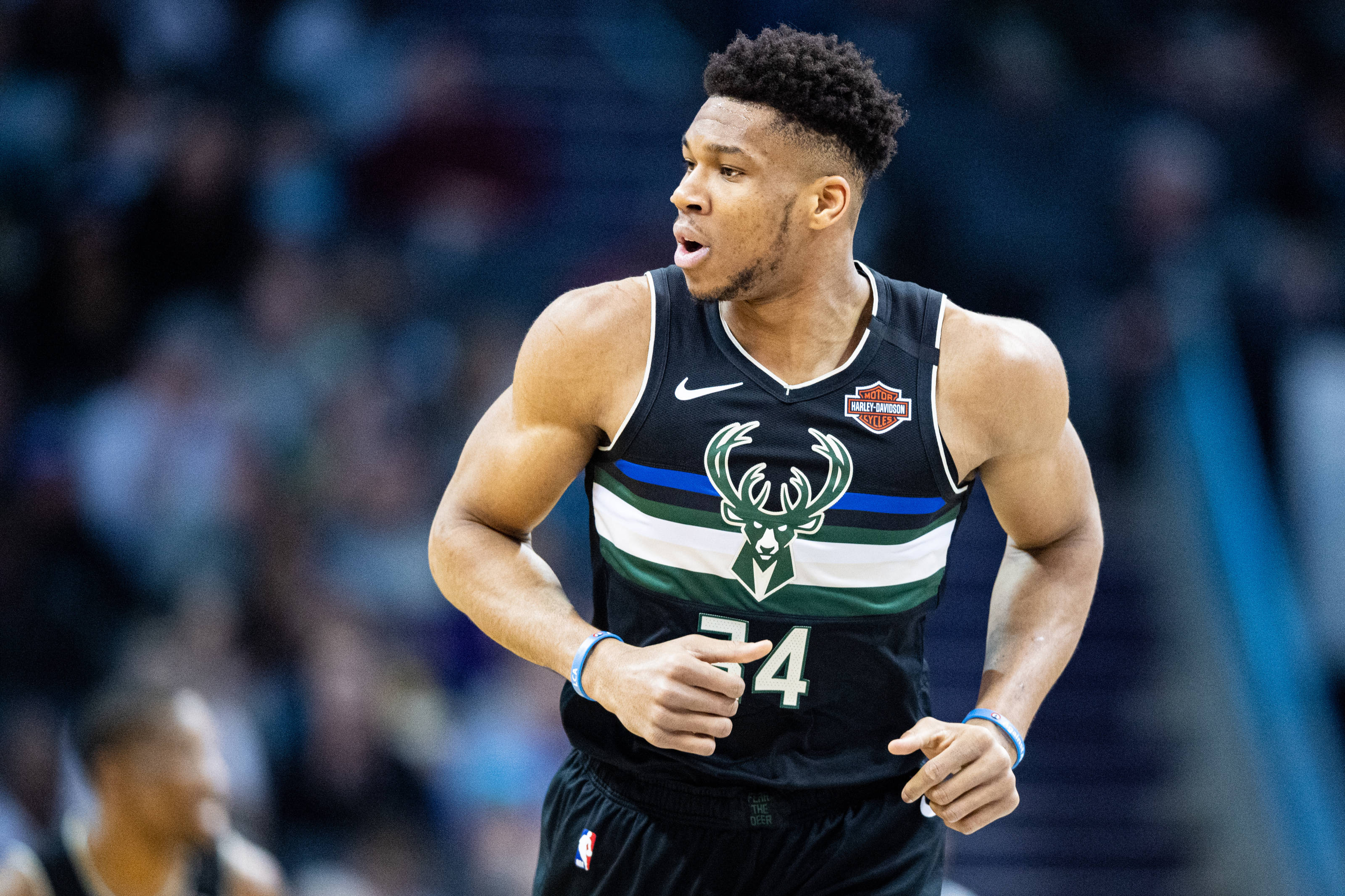 Giannis 桌布 壁紙 — 一位專注的籃球運動員身穿密爾瓦基公鹿隊球衣，在明亮的場館燈光下於激烈的比賽中衝刺。