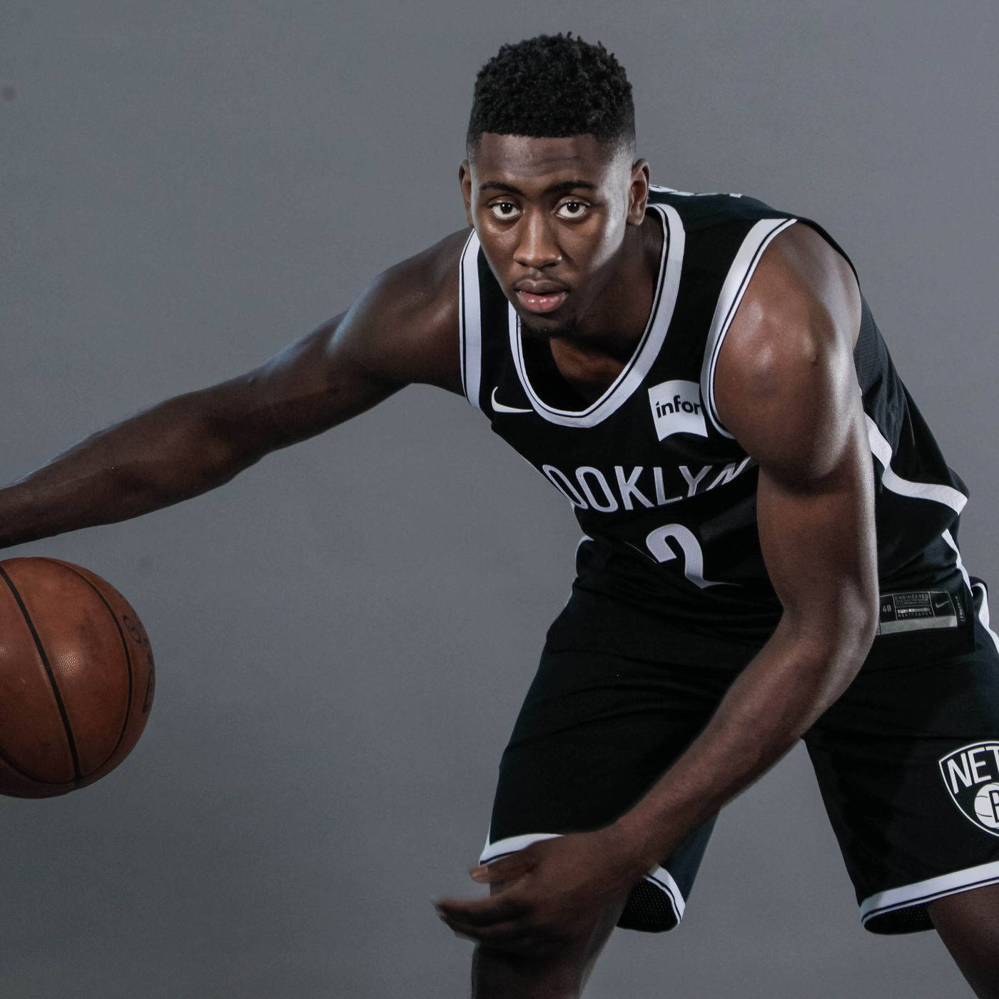 caris levert 桌布 壁紙 — 一位專注的籃球運動員身穿布魯克林籃網隊球衣，在純灰色工作室背景前運球。