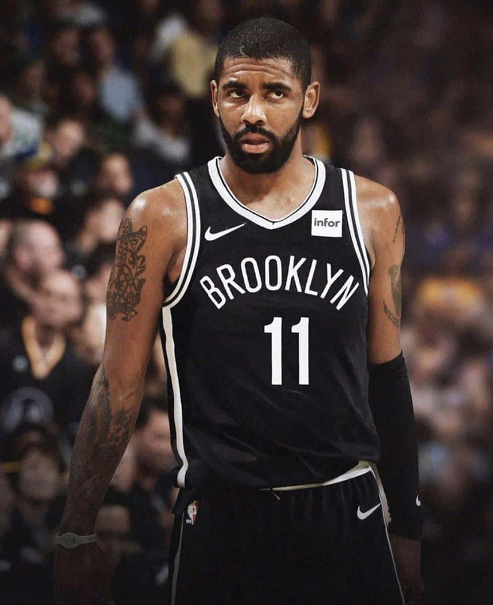 Kyrie Irving Nets 桌布 壁紙 — 一位專注的籃球運動員身穿布魯克林籃網隊球衣，站在球場上，身後是模糊的人群。