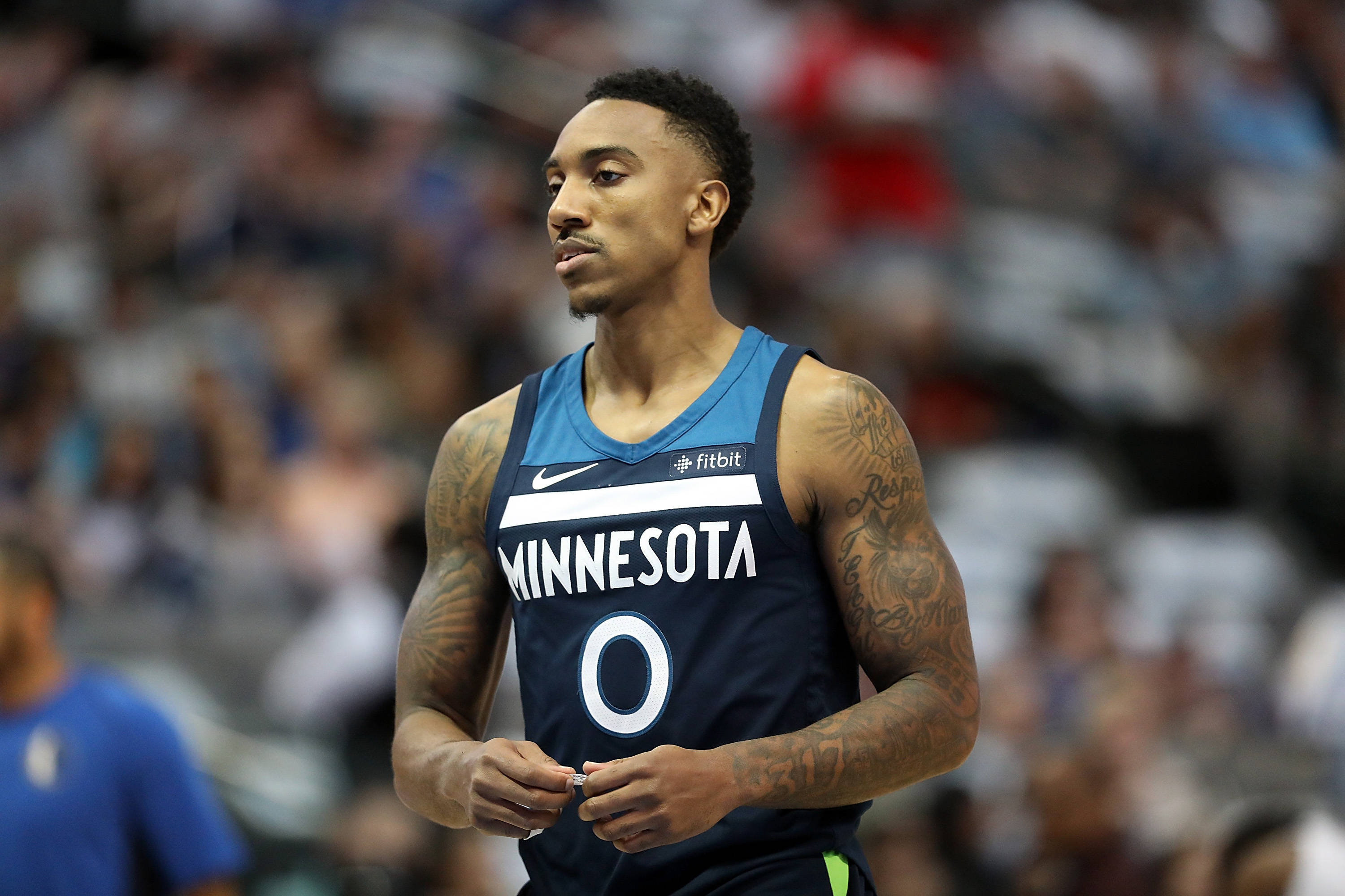 Timberwolves 桌布 壁紙 — 一位專注的籃球運動員身穿明尼蘇達球衣，帶有刺青，在比賽期間站在球場上，背景是模糊的觀眾。