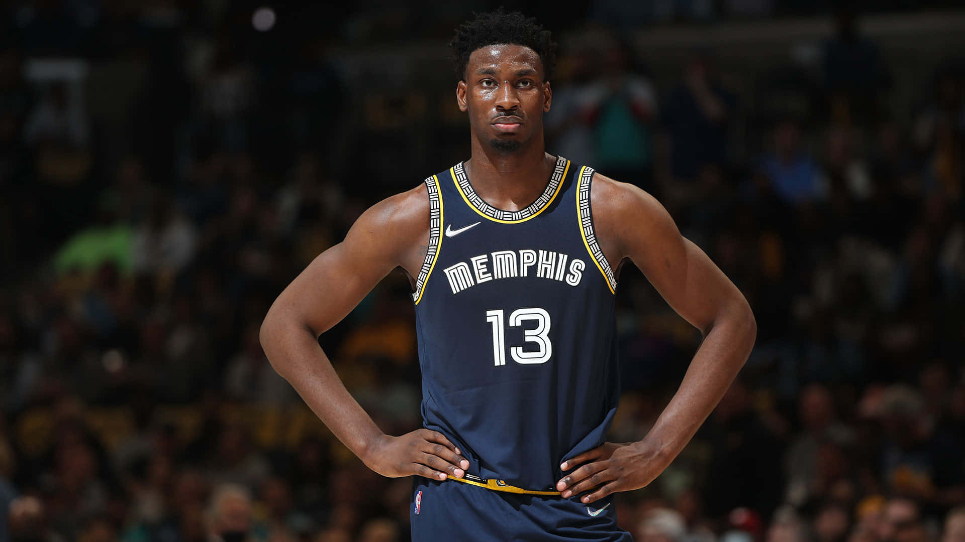 NBA 桌布 壁紙 — 一位專注的籃球運動員身穿曼菲斯灰熊隊球衣，在場館燈光下手叉腰站立。