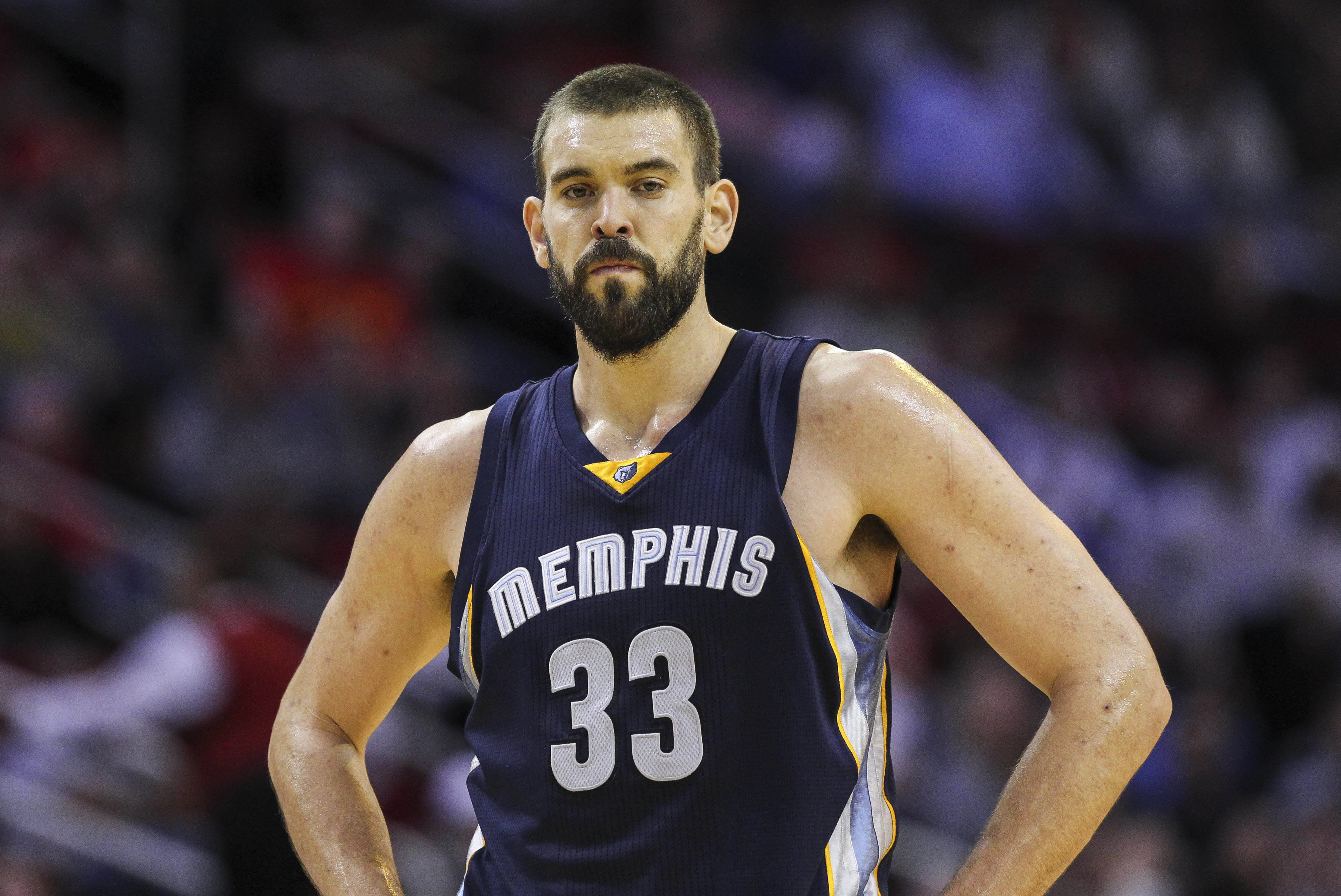 Marc Gasol 桌布 壁紙 — 一位專注的籃球運動員身穿曼菲斯球衣，在明亮的場館燈光下比賽時雙手叉腰站立。