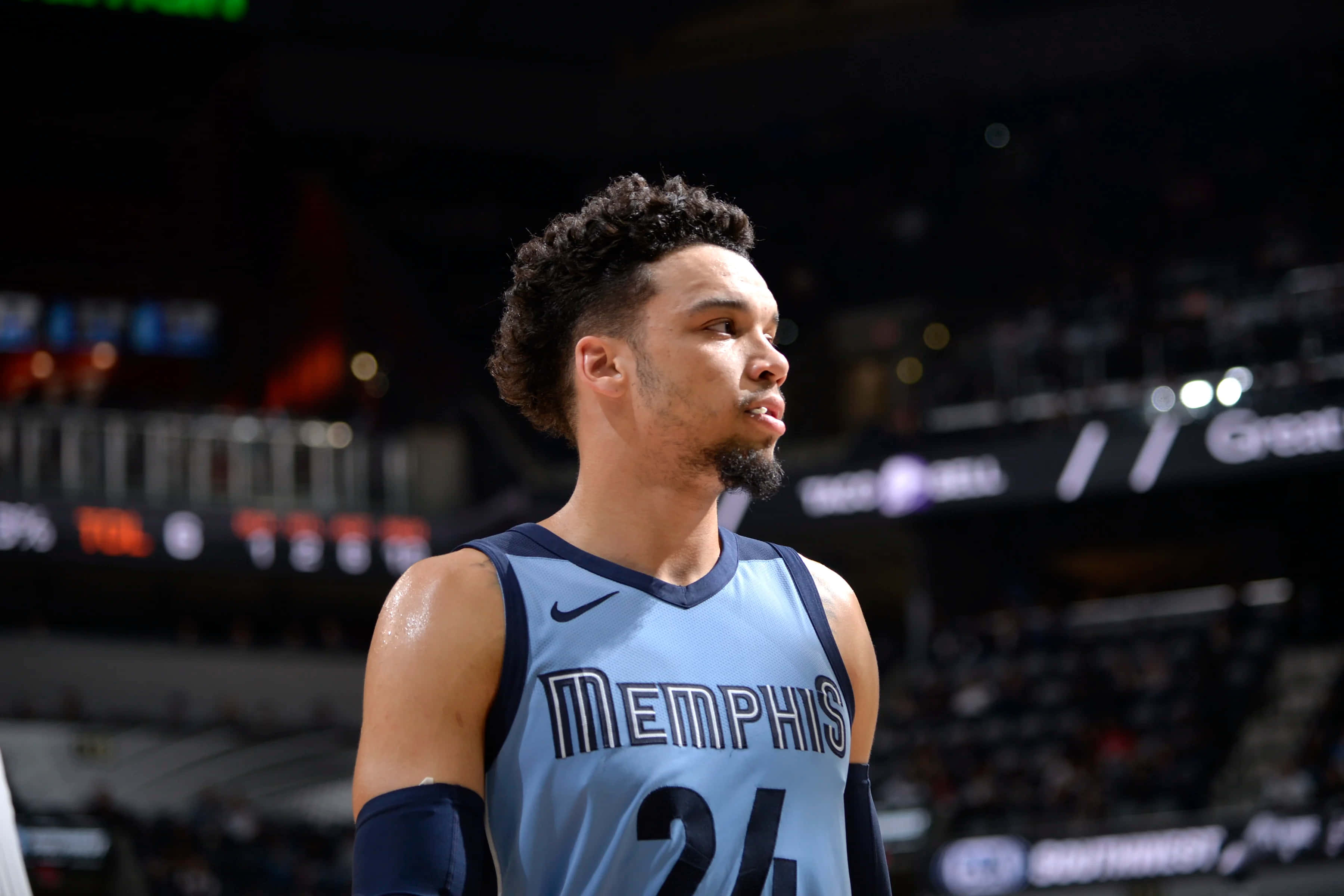 Dillon Brooks 桌布 壁紙 — 一位專注的籃球運動員身穿曼菲斯球衣，站在燈光明亮的球場上，背景是模糊的體育場燈光。