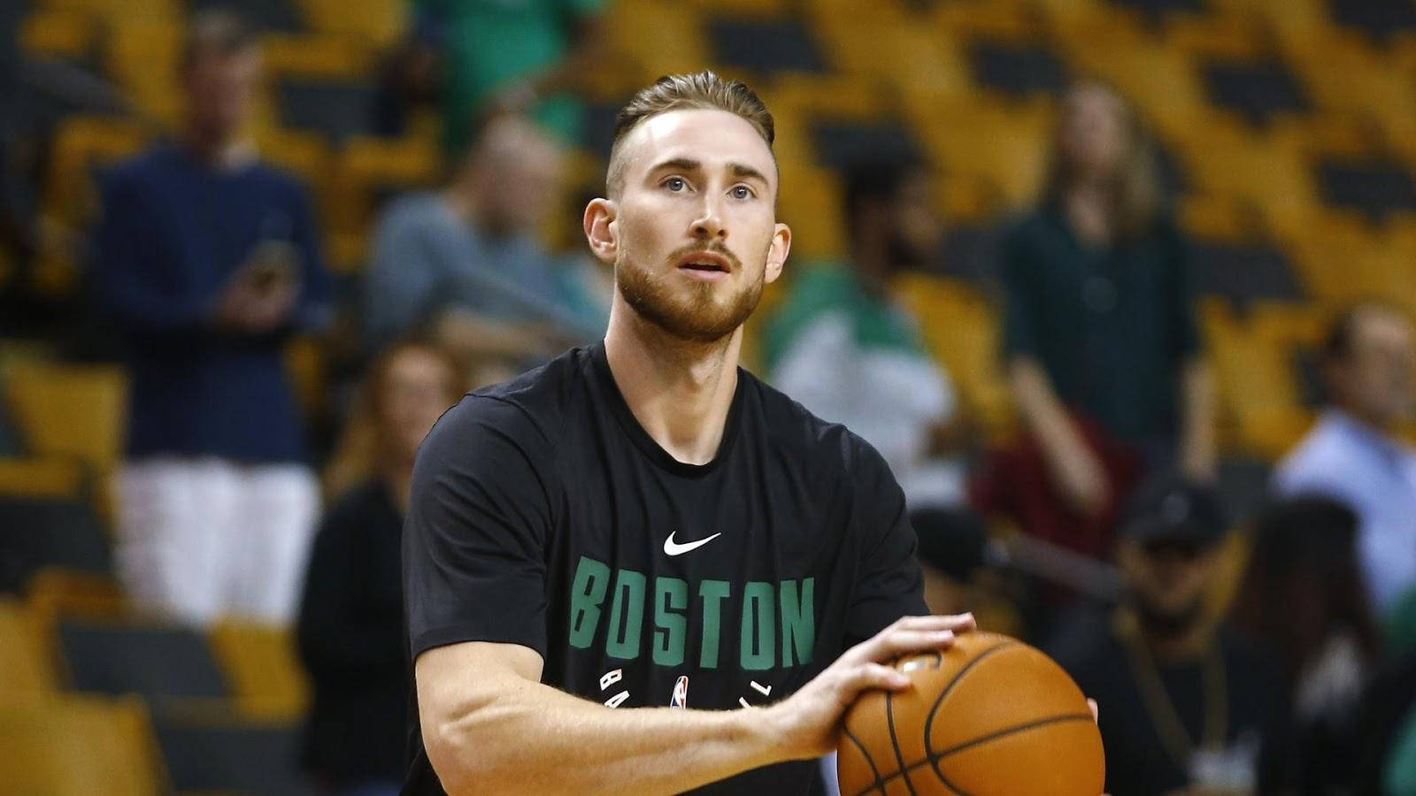 gordon hayward 桌布 壁紙 — 一位專注的籃球運動員身穿波士頓球衣，在練習中持球，背後黃色座位上的觀眾模糊不清。