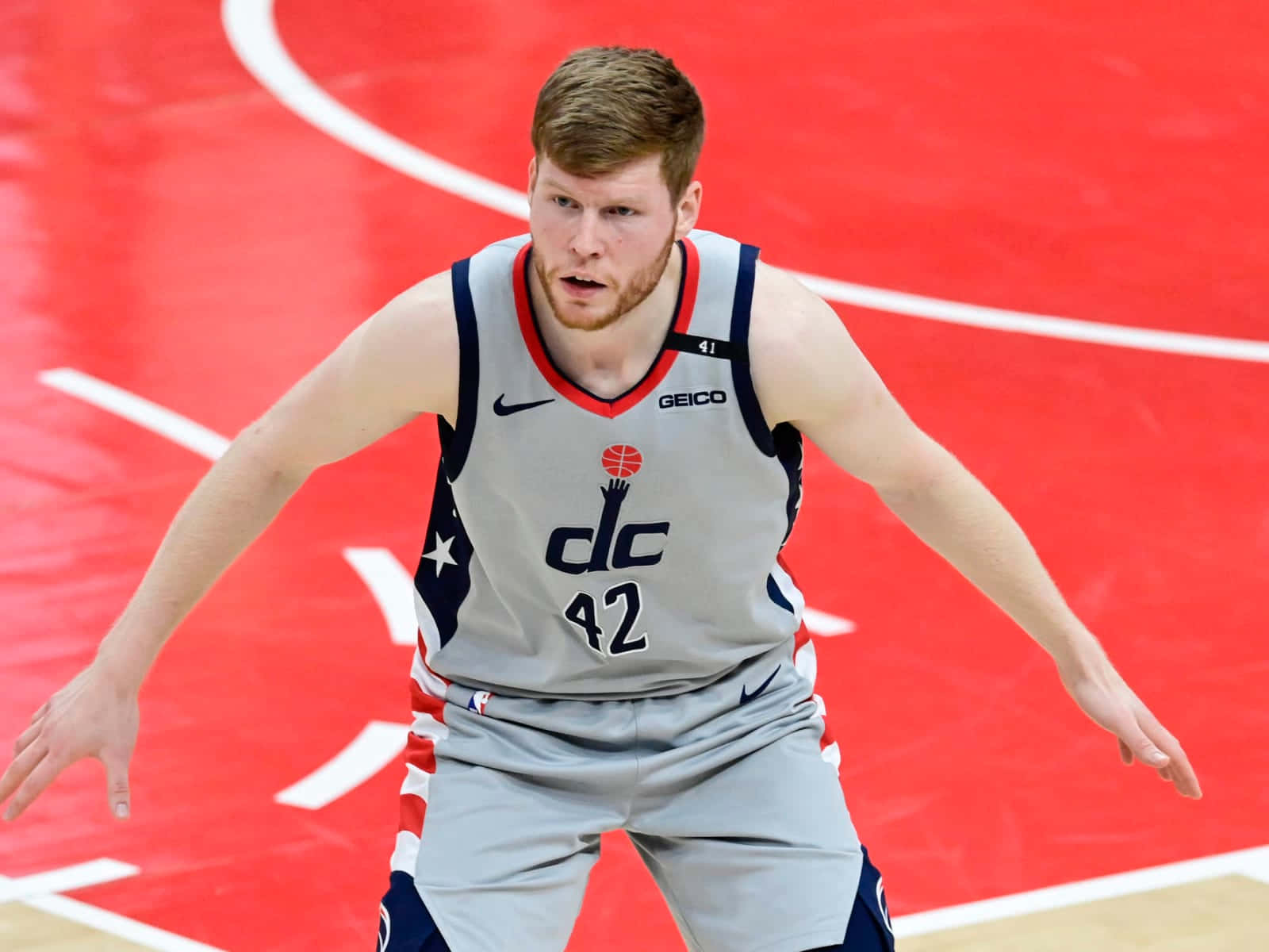 NBA 桌布 壁紙 — 一位專注的籃球運動員身穿灰色DC球衣，號碼42，站在充滿活力的紅色球場上。