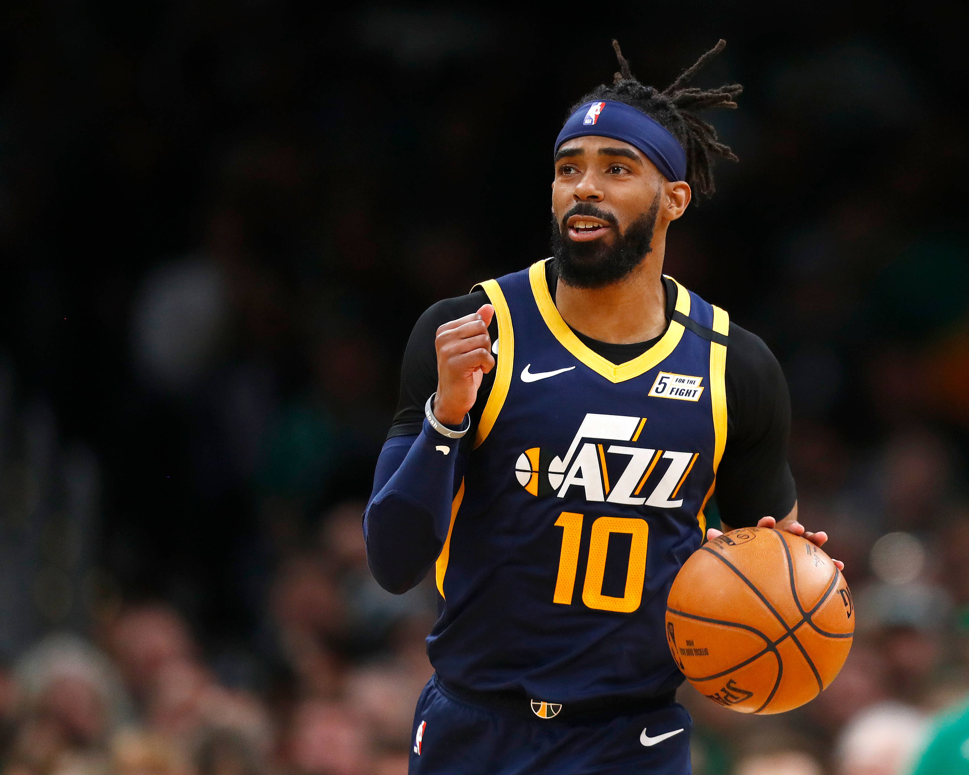 mike conley 桌布 壁紙 — 一位專注的籃球運動員身穿爵士隊球衣，在比賽中運球，身後是模糊的人群。