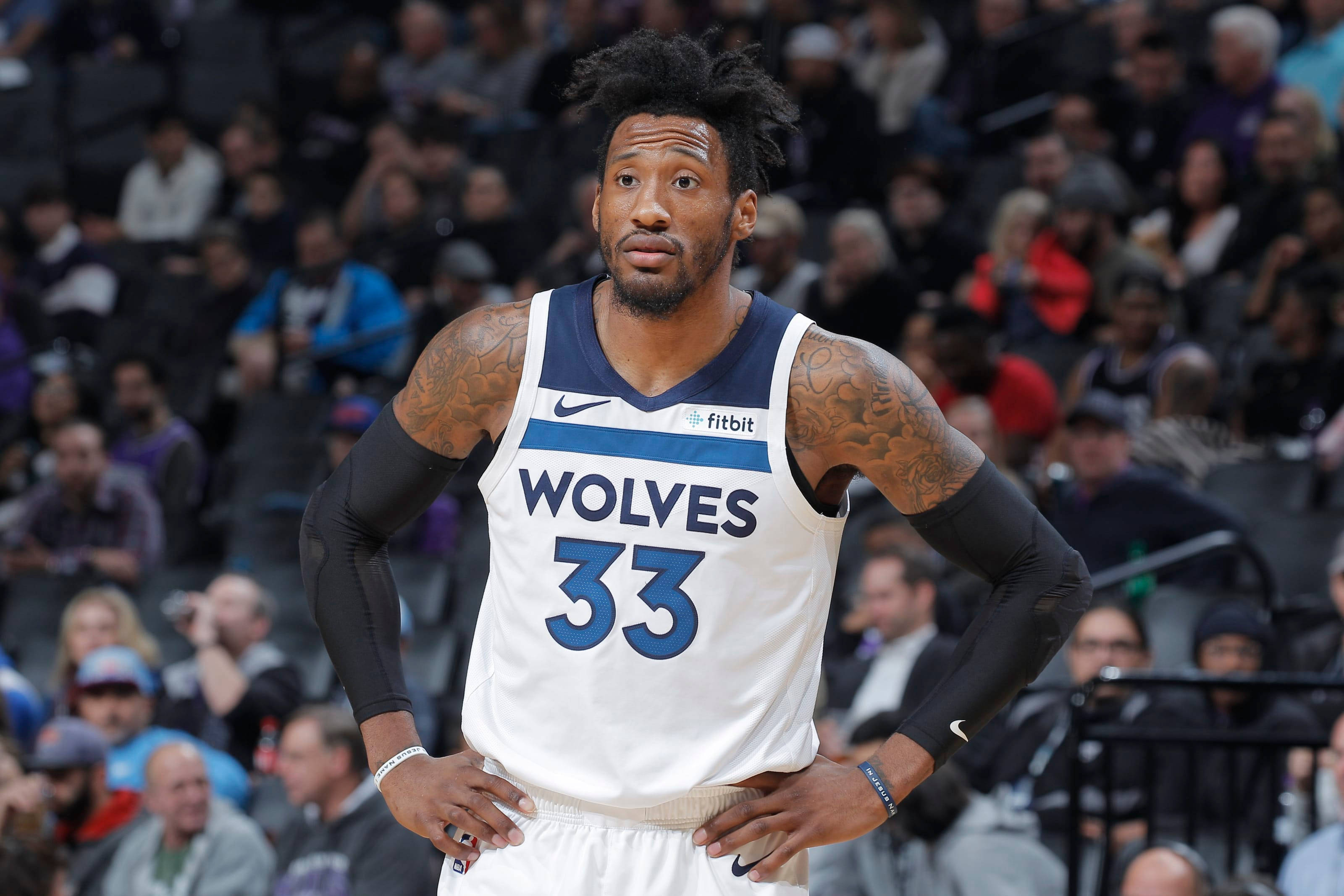 robert covington 桌布 壁紙 — 一位專注的籃球運動員身穿狼隊球衣，在比賽中雙手叉腰站立，背景有模糊的觀眾。