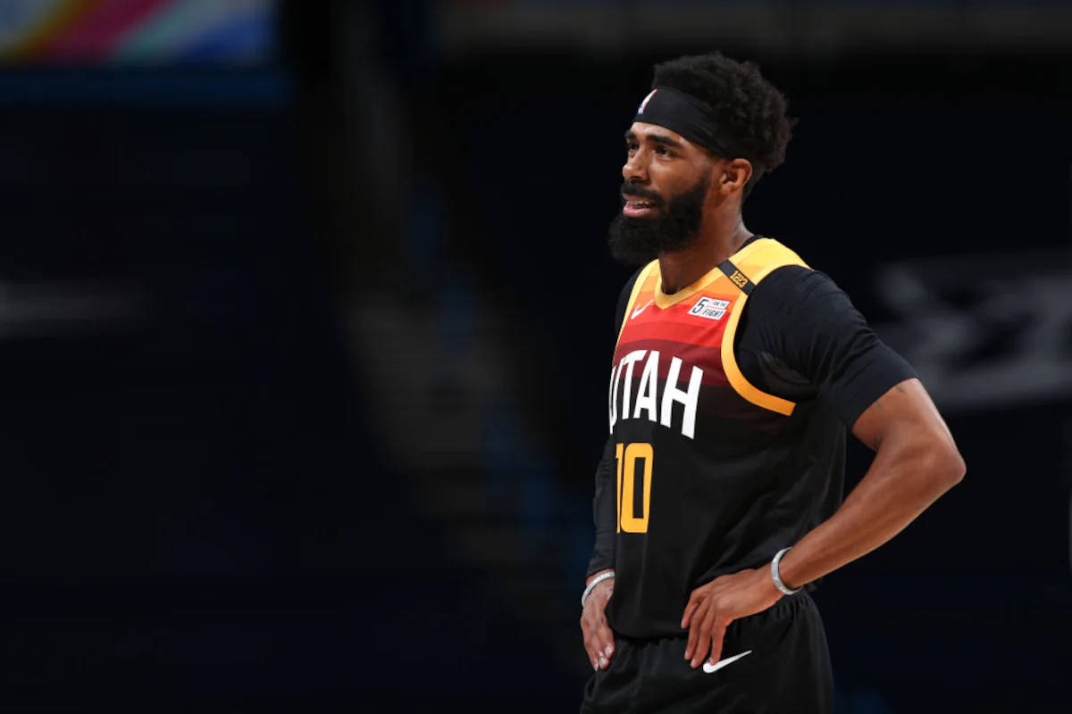 mike conley 桌布 壁紙 — 一位專注的籃球運動員身穿猶他爵士隊球衣，雙手叉腰站在燈光昏暗的球場上。