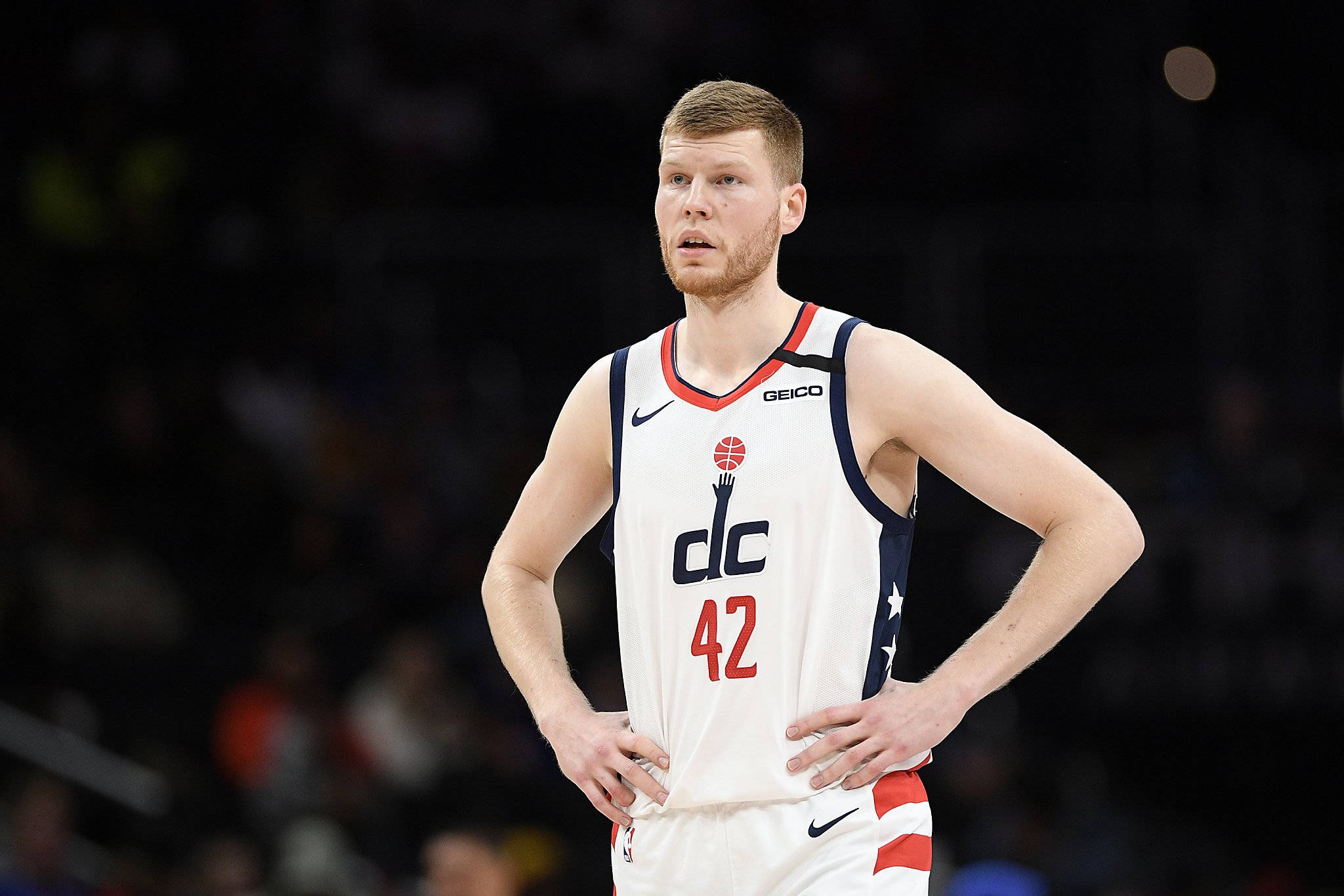 Wizards 桌布 壁紙 — 一位專注的籃球運動員身穿白色DC 42球衣，在明亮的場館燈光下比賽期間雙手叉腰站立。