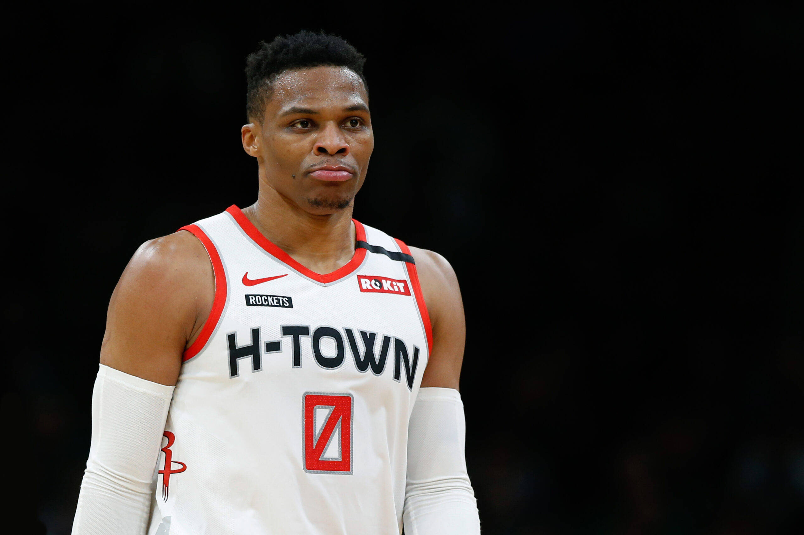 Westbrook 桌布 壁紙 — 一位專注的籃球運動員身穿白色H-Town球衣，帶有紅色點綴，站在深色背景前。
