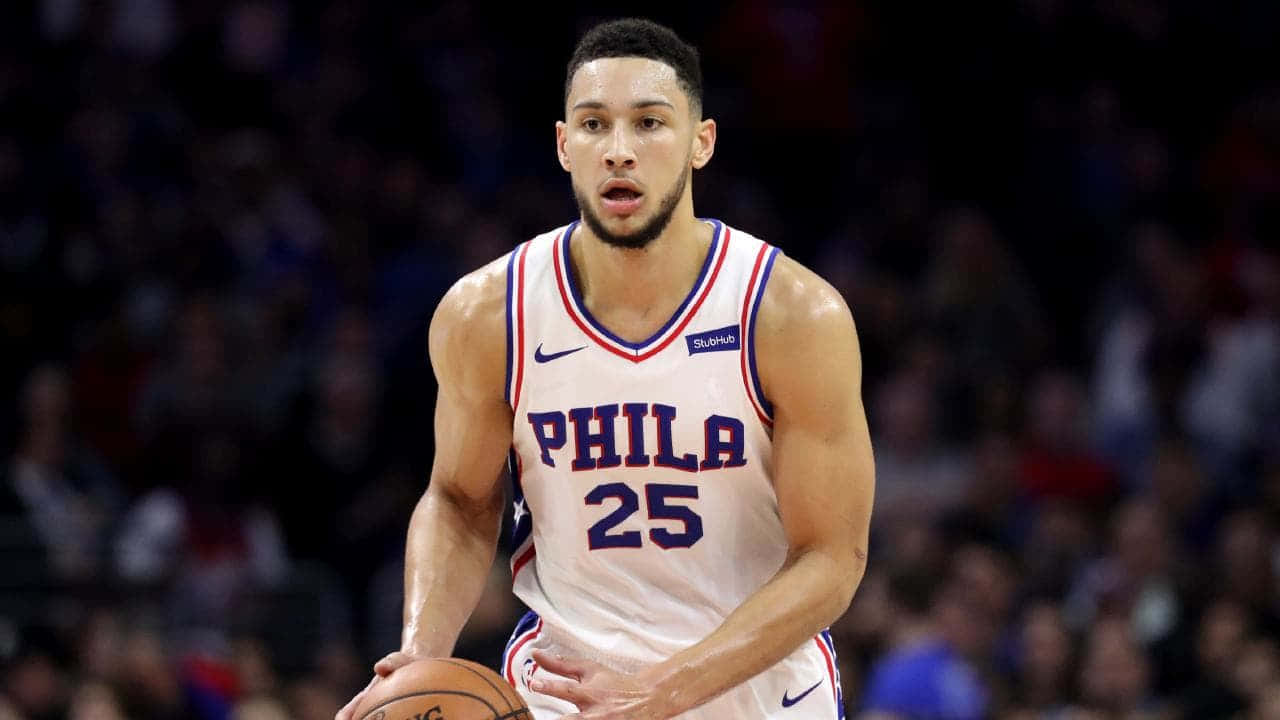 Nba2k20 桌布 壁紙 — 一位專注的籃球運動員身穿白色Phila球衣，在明亮的場館燈光下於激烈比賽中運球。