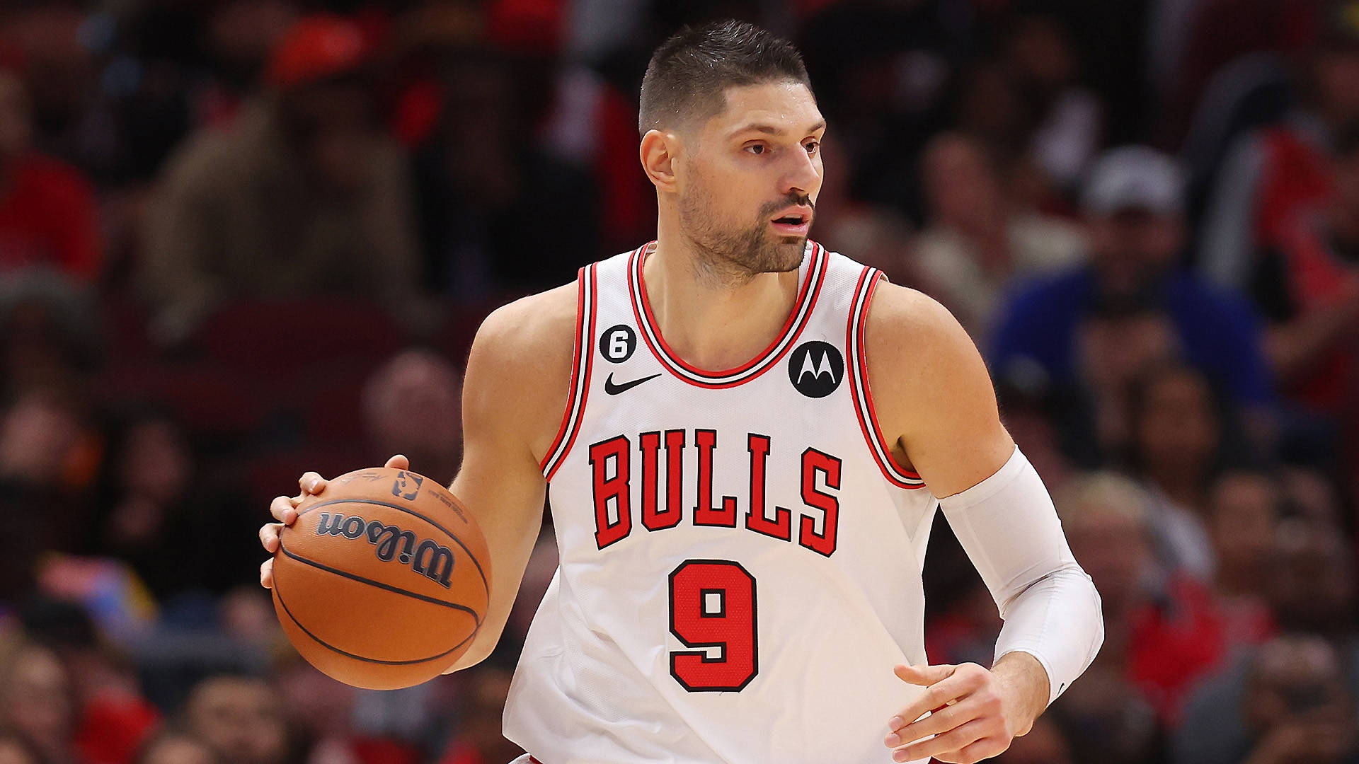 NBA 桌布 壁紙 — 一位專注的籃球運動員身穿白色公牛隊球衣，在明亮的場館燈光下於激烈的比賽中運著威爾森球。
