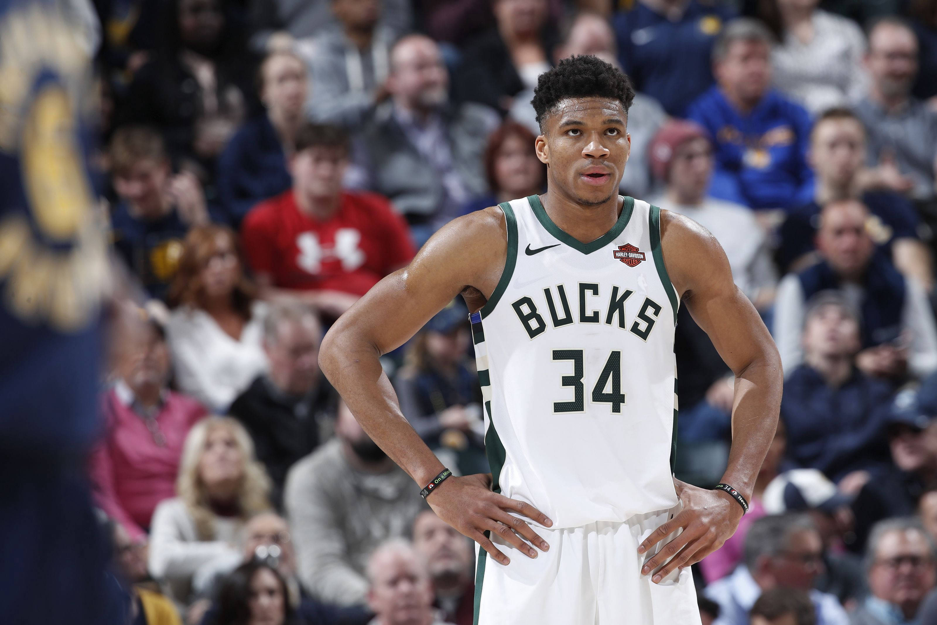Giannis 桌布 壁紙 — 一位專注的籃球運動員身穿白色公鹿隊34號球衣，雙手叉腰站在比賽中，背景是模糊的觀眾。