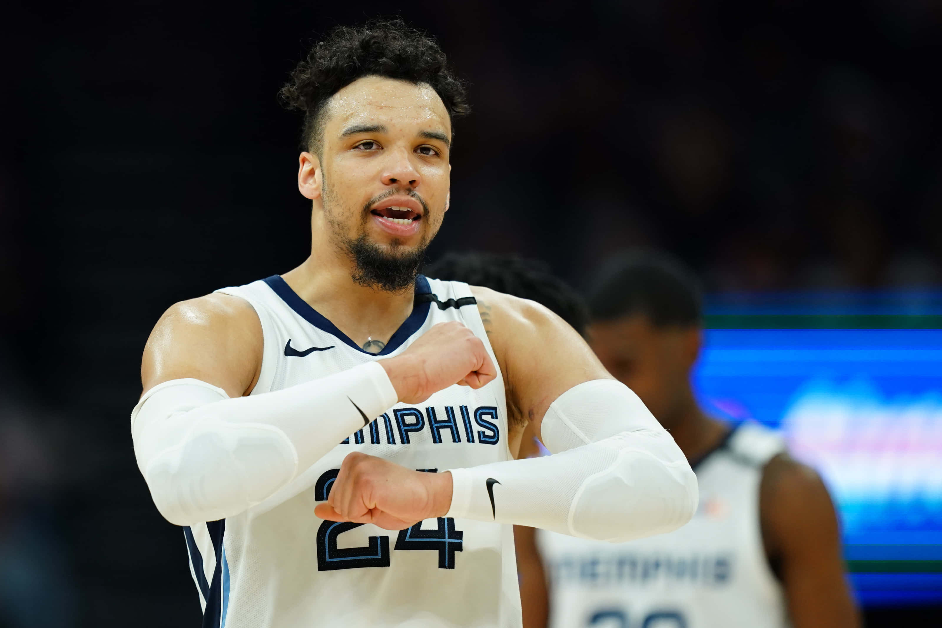 Dillon Brooks 桌布 壁紙 — 一位專注的籃球運動員身穿白色曼菲斯球衣（24號），在明亮的場館燈光下比賽時彎曲雙臂。
