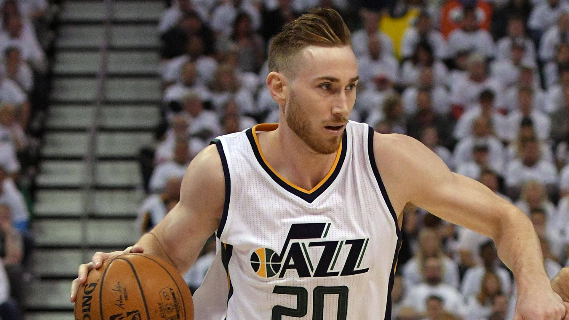 gordon hayward 桌布 壁紙 — 一位專注的籃球運動員身穿白色爵士隊球衣，在模糊的人群背景下進行激烈的比賽運球。