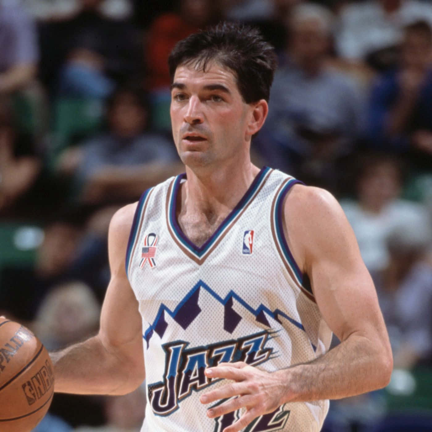 NBA 桌布 壁紙 — 一位專注的籃球運動員身穿白色爵士隊球衣，在激烈的比賽中運球，背景是模糊的觀眾。