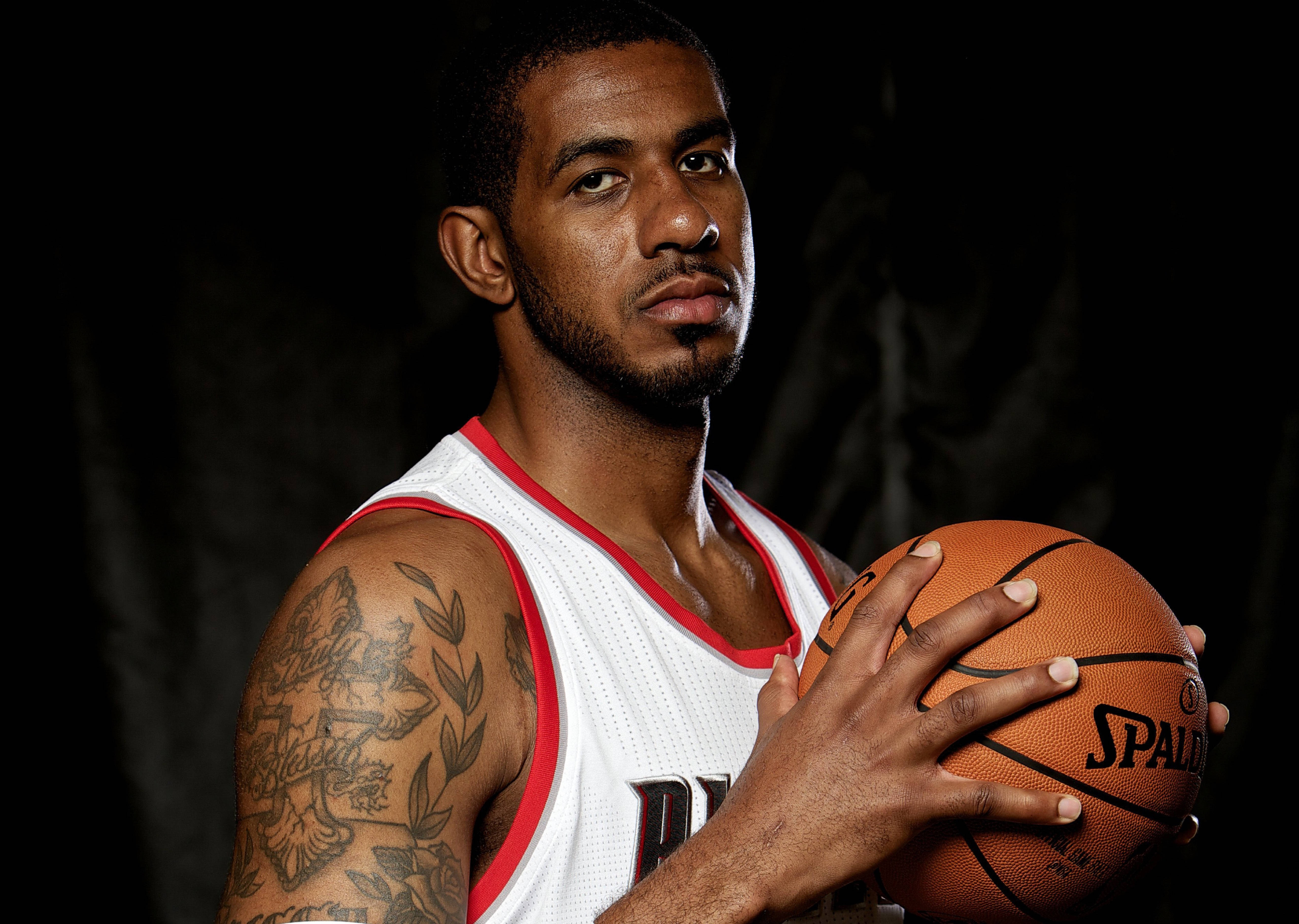 Lamarcus Aldridge 桌布 壁紙 — 一位專注的籃球運動員身穿白色球衣，在黑暗的攝影棚背景下拿著 Spalding 籃球，手臂上有明顯的刺青。