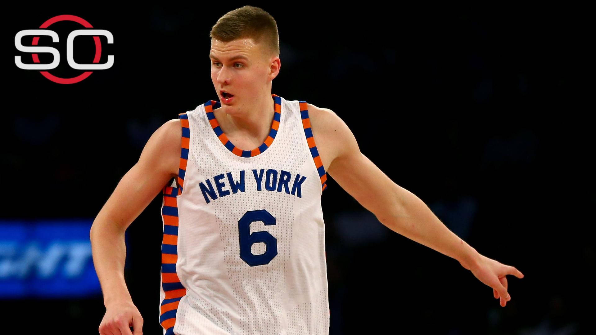 Kristaps Porzingis 桌布 壁紙 — 一位專注的籃球運動員身穿紐約尼克隊6號球衣，在明亮的場館燈光下比賽中激烈地做手勢。