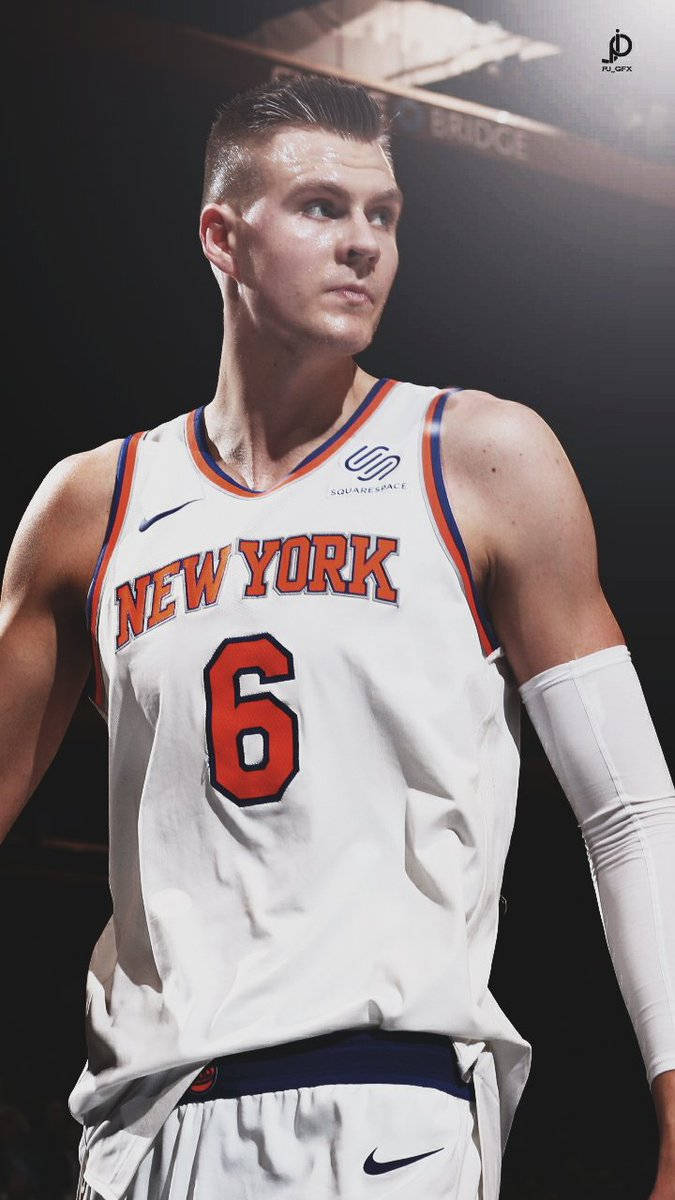 Kristaps Porzingis 桌布 壁紙 — 一位專注的籃球運動員身穿紐約尼克隊6號球衣，站在戲劇性的場館燈光下。
