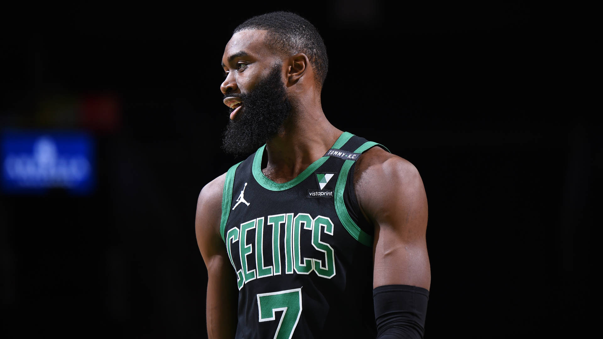 Jaylen Brown 桌布 壁紙 — 一位專注的籃球運動員身穿綠色和黑色的塞爾提克球衣，站在黑暗的球場背景下。