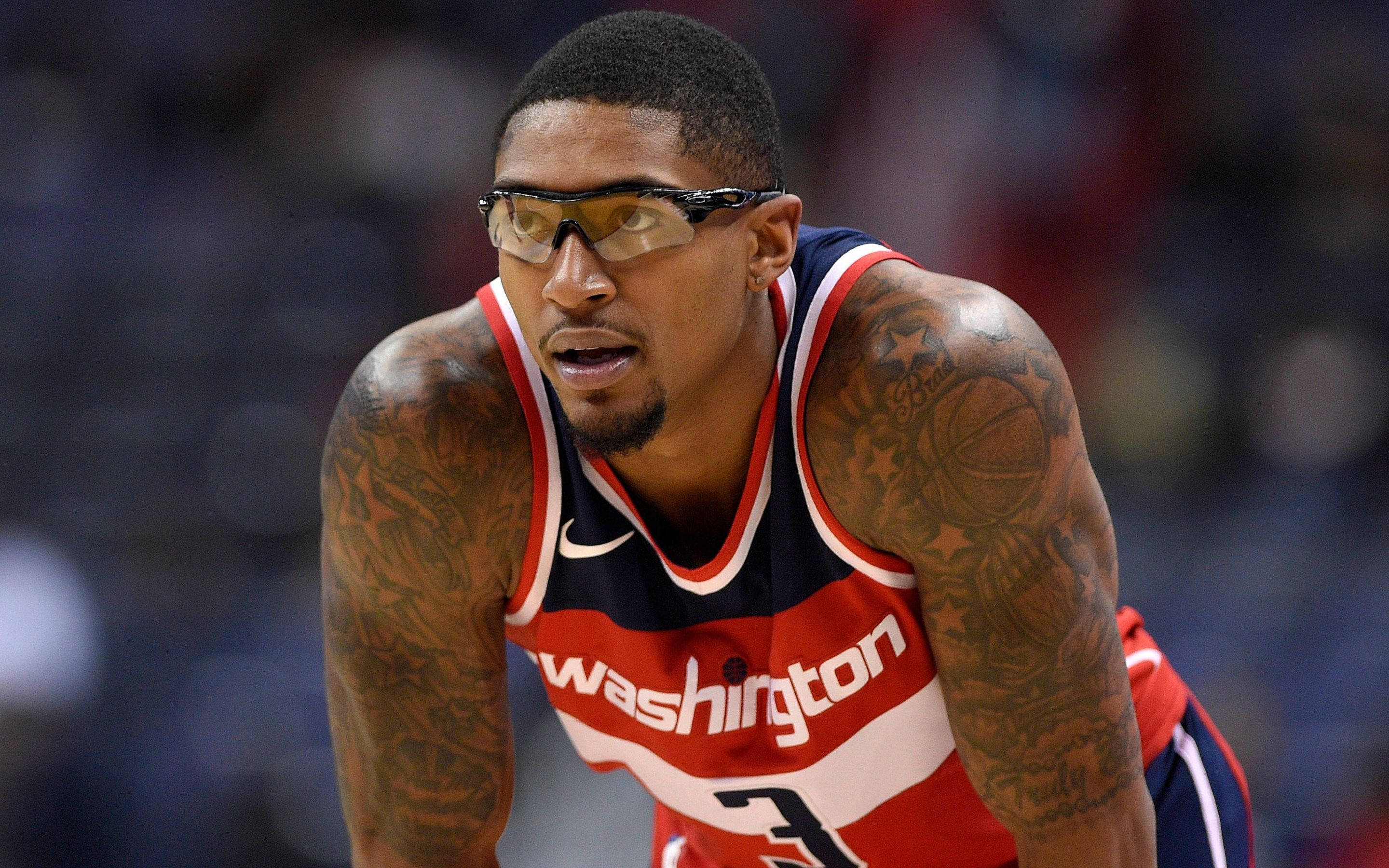Bradley Beal 桌布 壁紙 — 一位專注的籃球運動員身穿華盛頓球衣，帶有刺青和護目鏡，在比賽中向前傾。