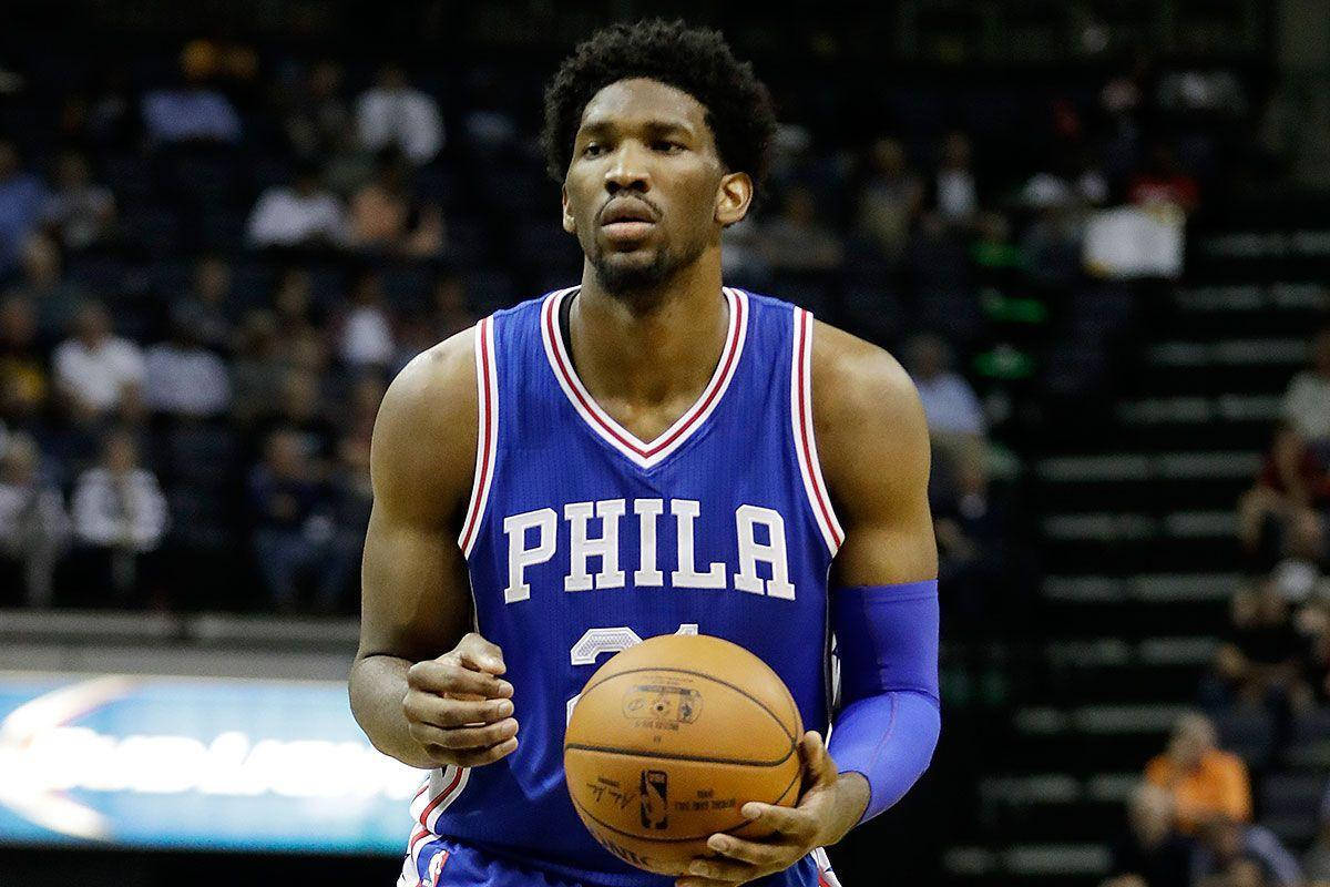 Embiid 桌布 壁紙 — 一位專注的籃球運動員身穿藍色 'PHILA' 球衣，在場館燈光下於比賽中持球。