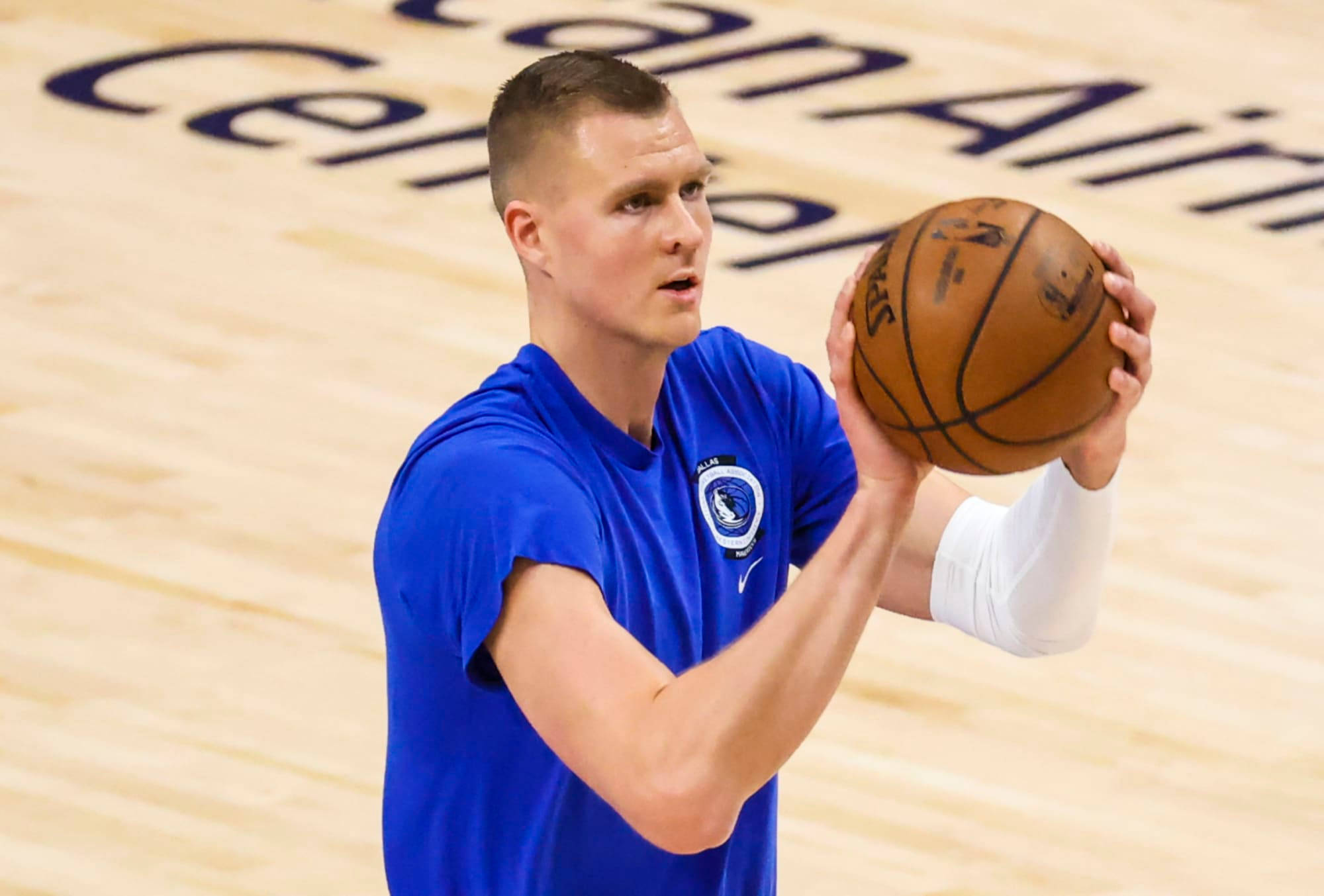 Kristaps Porzingis 桌布 壁紙 — 一位專注的籃球運動員身穿藍色球衣，準備在拋光木地板上投籃。