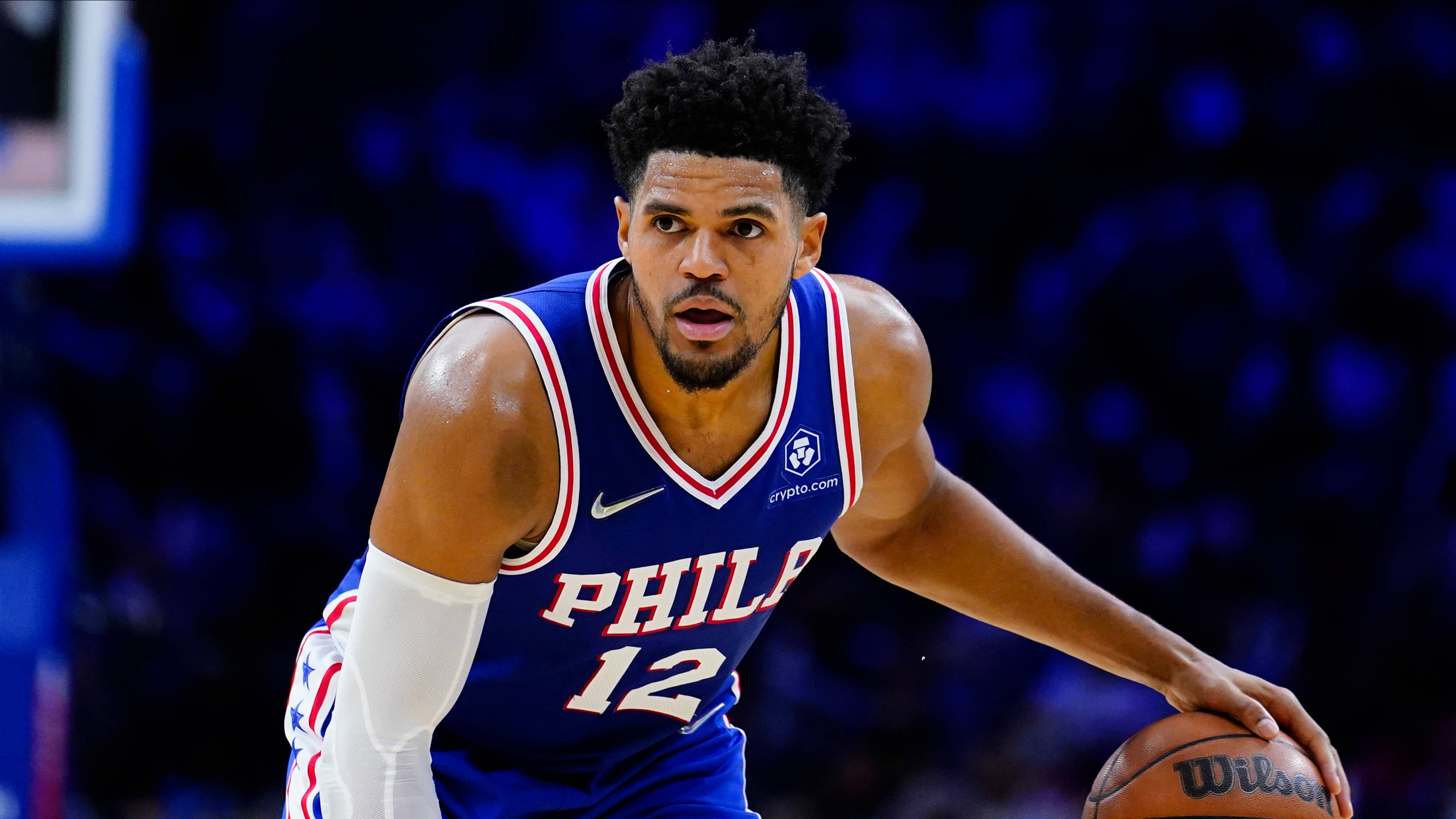 NBA 桌布 壁紙 — 一位專注的籃球運動員身穿藍色費城球衣，在明亮的場館燈光下激烈運球。