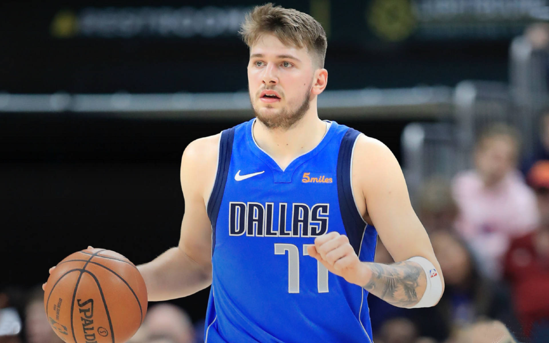 Luka 桌布 壁紙 — 一位專注的籃球運動員身穿藍色達拉斯球衣，在明亮的場館燈光下於激烈的比賽中運球。