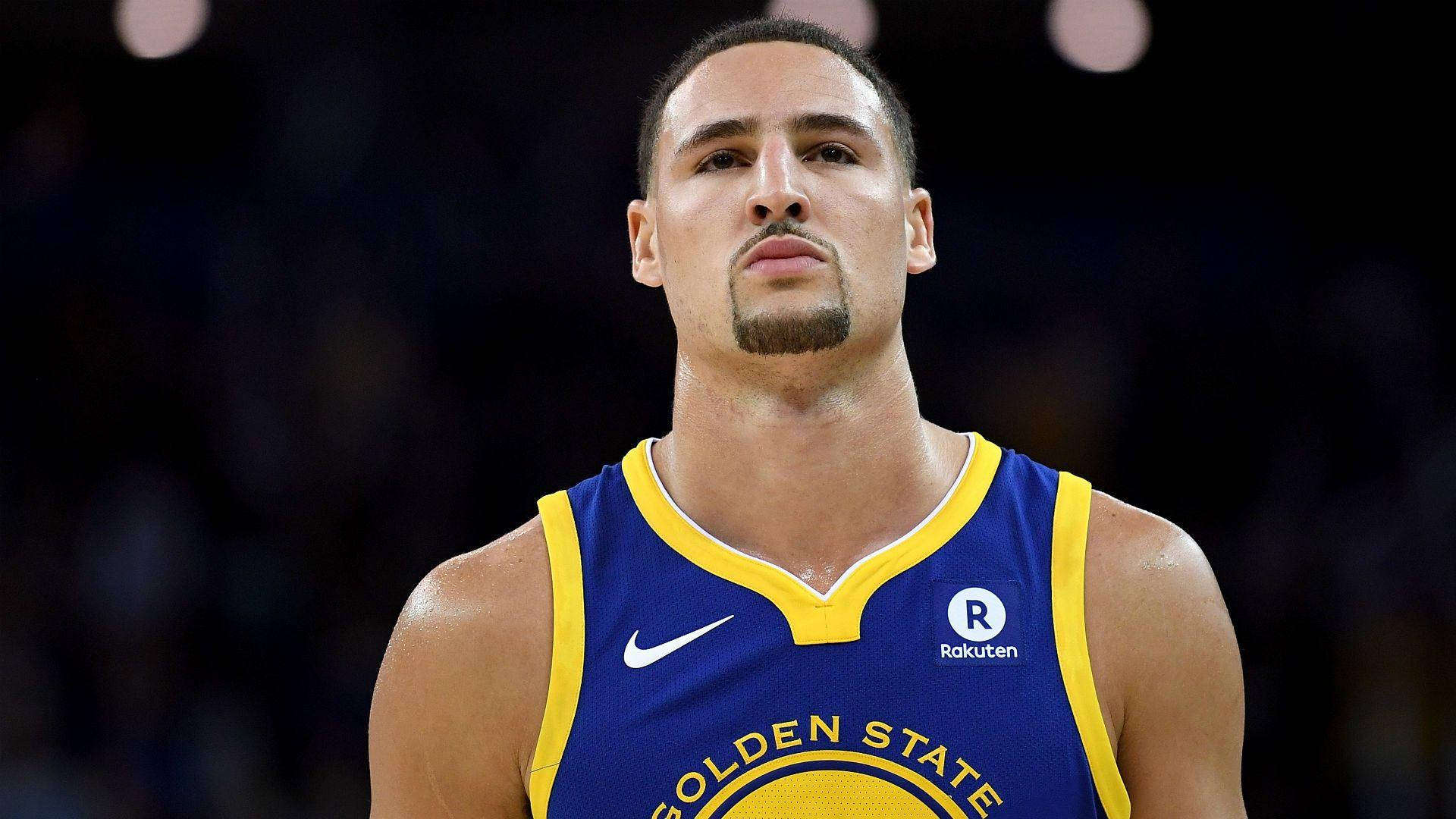 Thompson 桌布 壁紙 — 一位專注的籃球運動員身穿藍黃色金州勇士隊球衣，在明亮的場館燈光下比賽中凝視著。