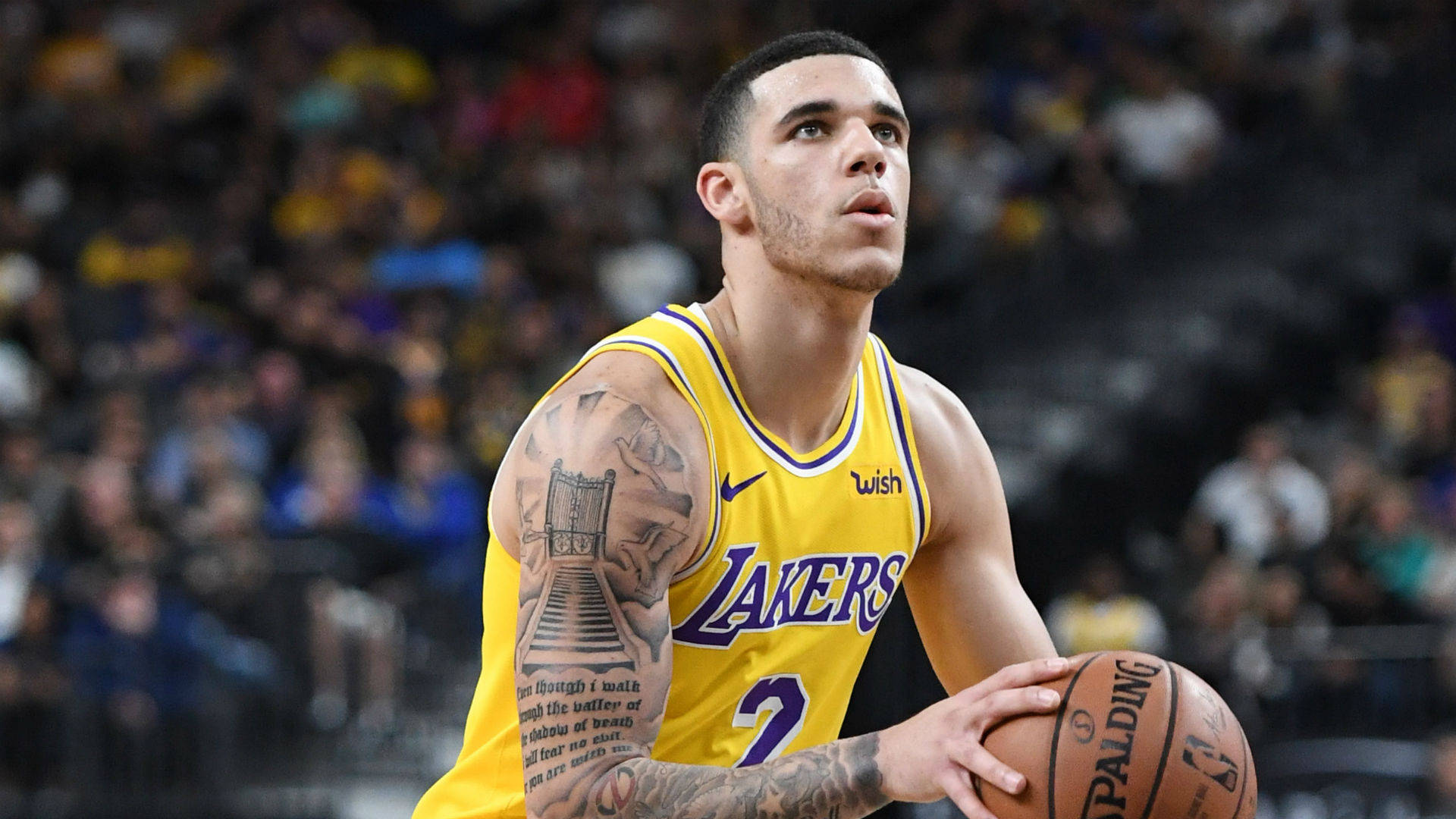 NBA 桌布 壁紙 — 一位專注的籃球運動員身穿黃色湖人隊球衣，在比賽中手持Spalding籃球，手臂上可見刺青。