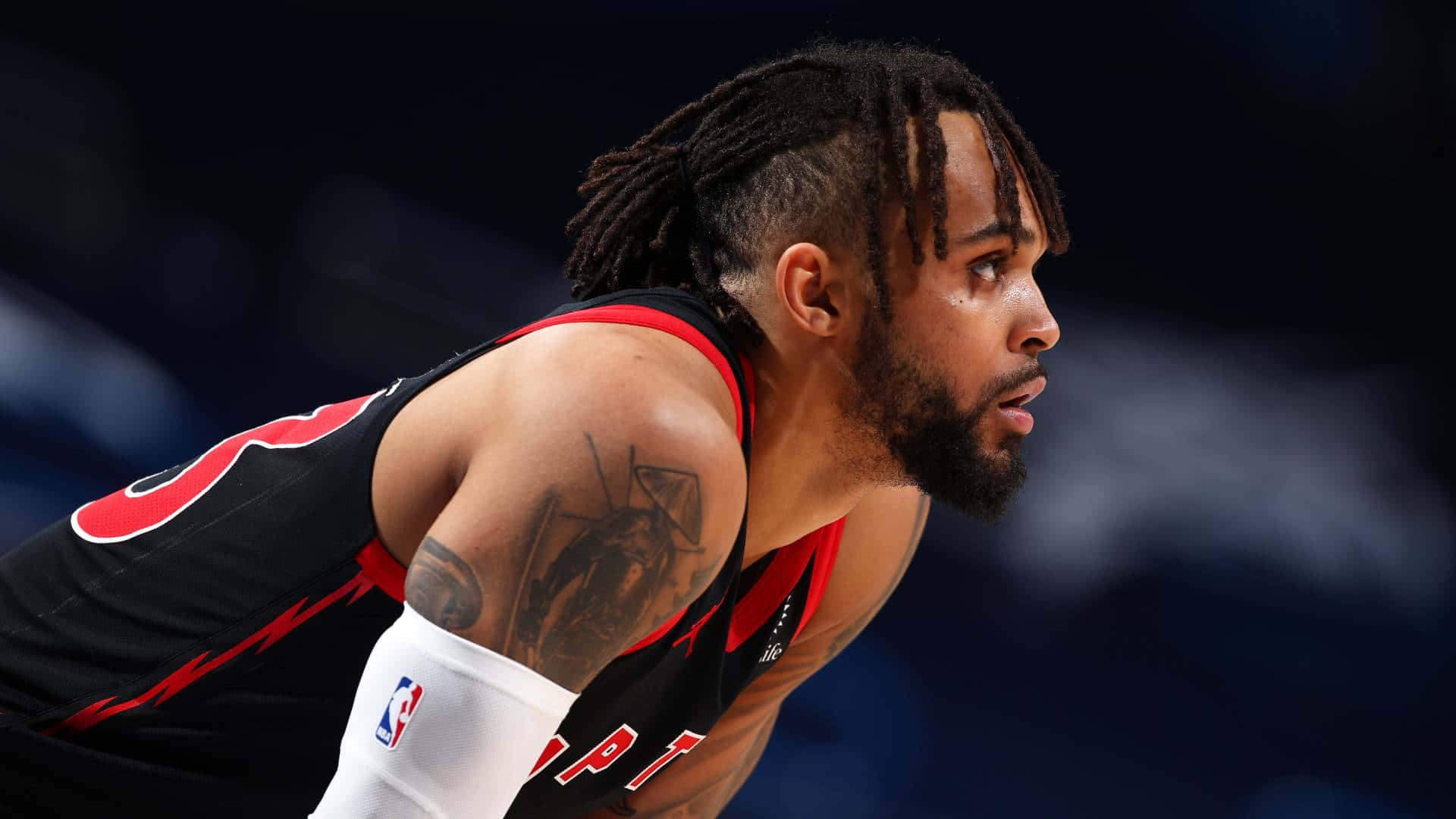 NBA 桌布 壁紙 — 一位專注的籃球運動員身穿黑紅色球衣，在明亮的場館燈光下比賽中身體前傾，目光專注。