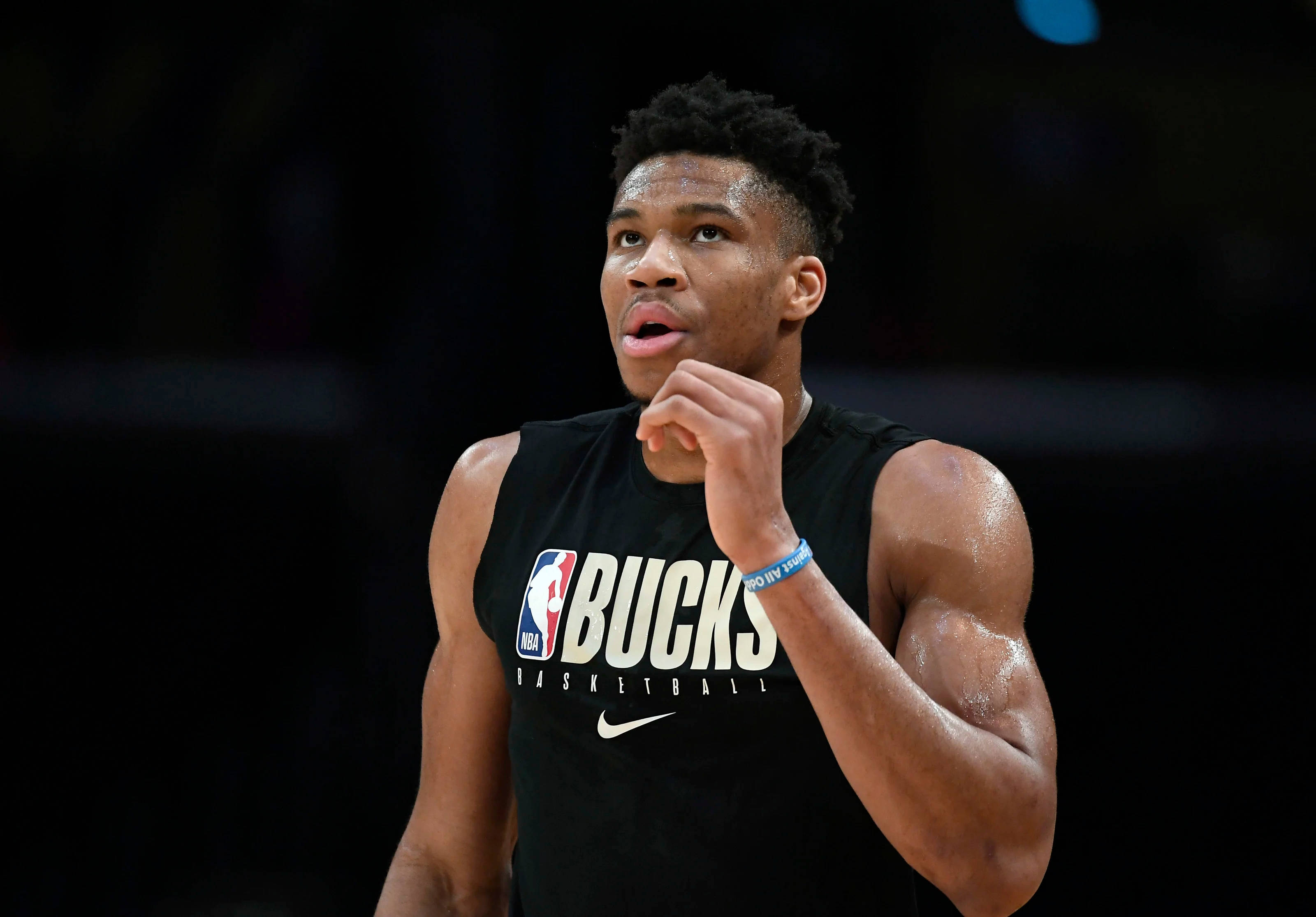 Giannis 桌布 壁紙 — 一位專注的籃球運動員身穿黑色公鹿隊球衣，在比賽中於場館燈光下抓著下巴。