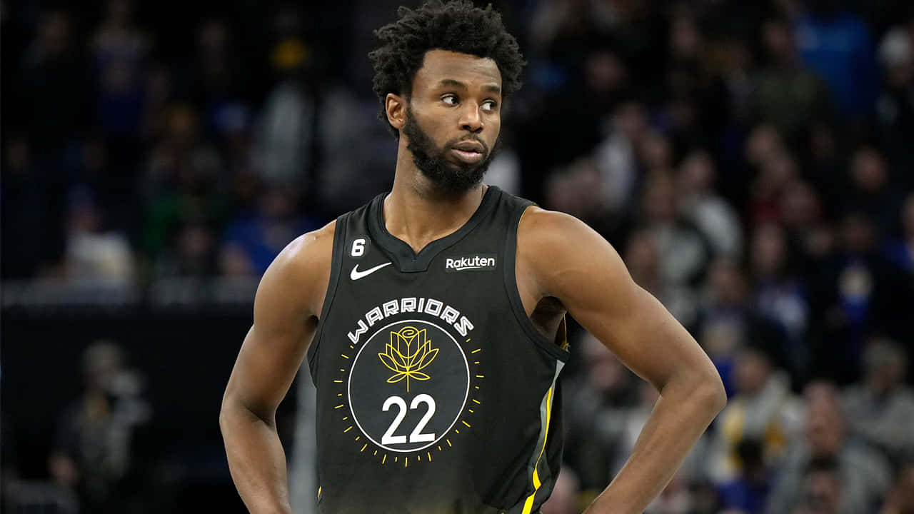 Andrew Wiggins 桌布 壁紙 — 一位專注的籃球運動員身穿黑色勇士隊22號球衣，站在球場上，背景是模糊的觀眾。