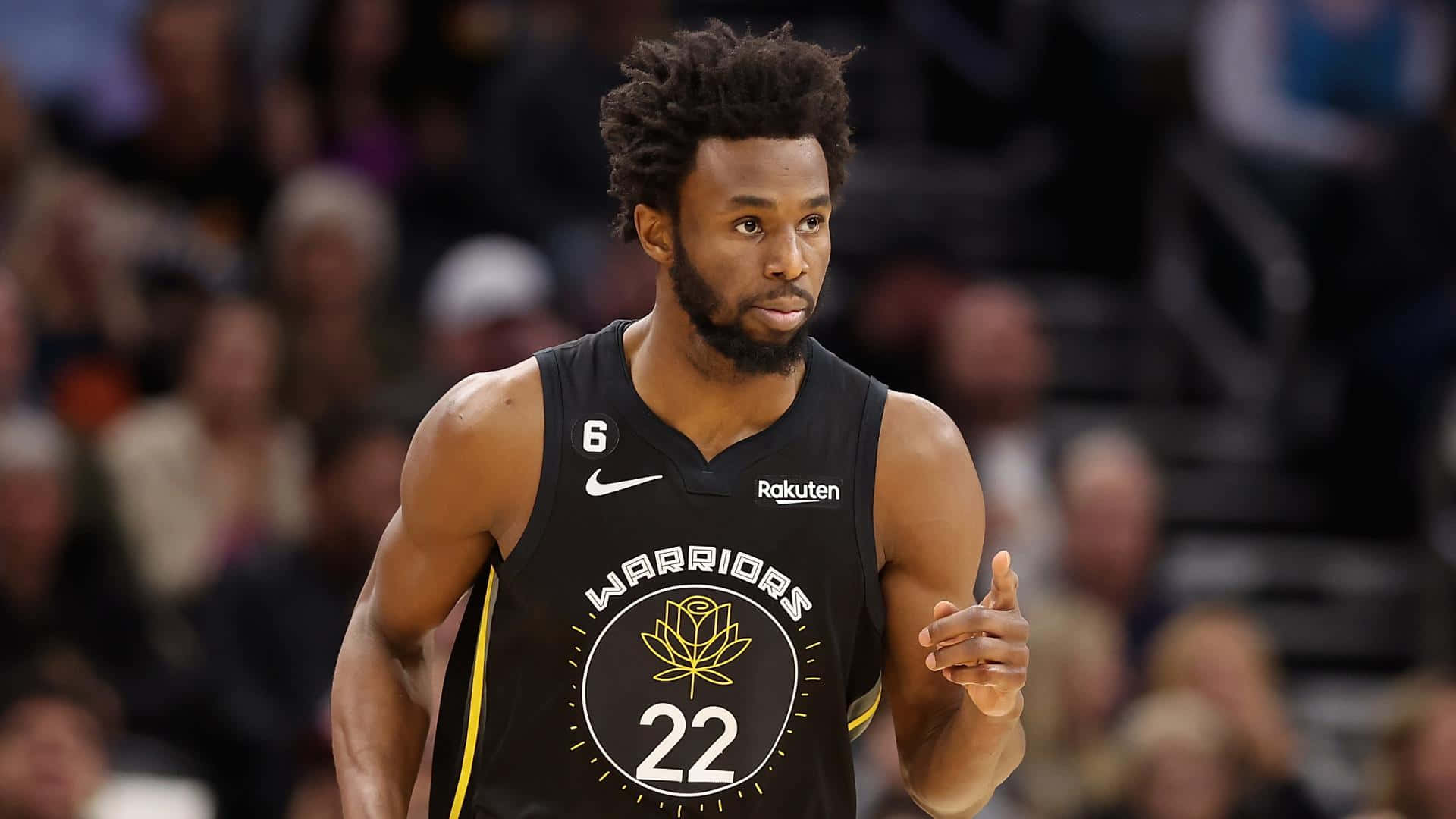 Andrew Wiggins 桌布 壁紙 — 一位專注的籃球運動員身穿黑色勇士隊22號球衣，在明亮的場館燈光下比賽中做手勢。