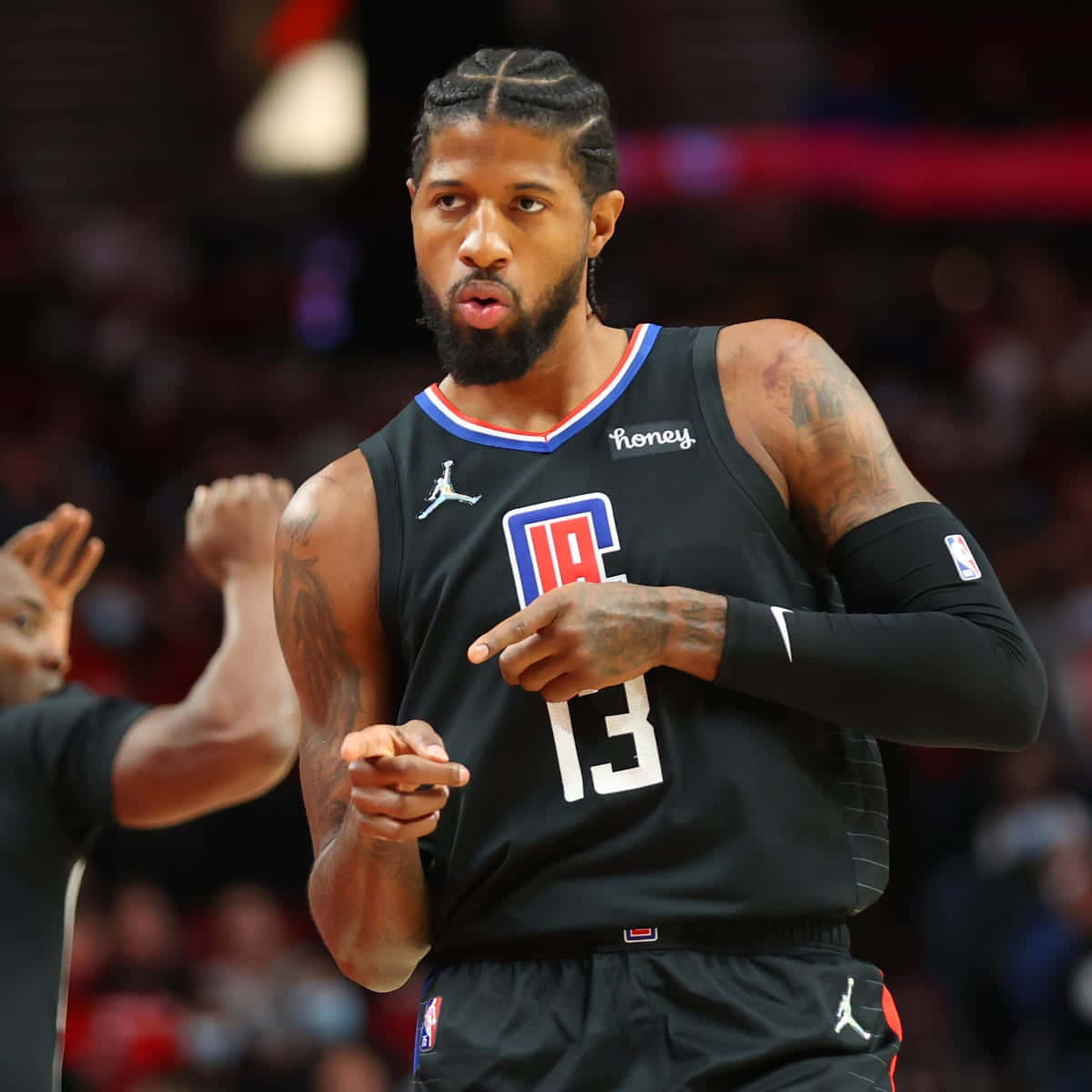Paul George Clippers 桌布 壁紙 — 一位專注的籃球運動員身穿黑色快艇隊球衣，號碼13，在明亮的場館燈光下比賽中激烈地做手勢。