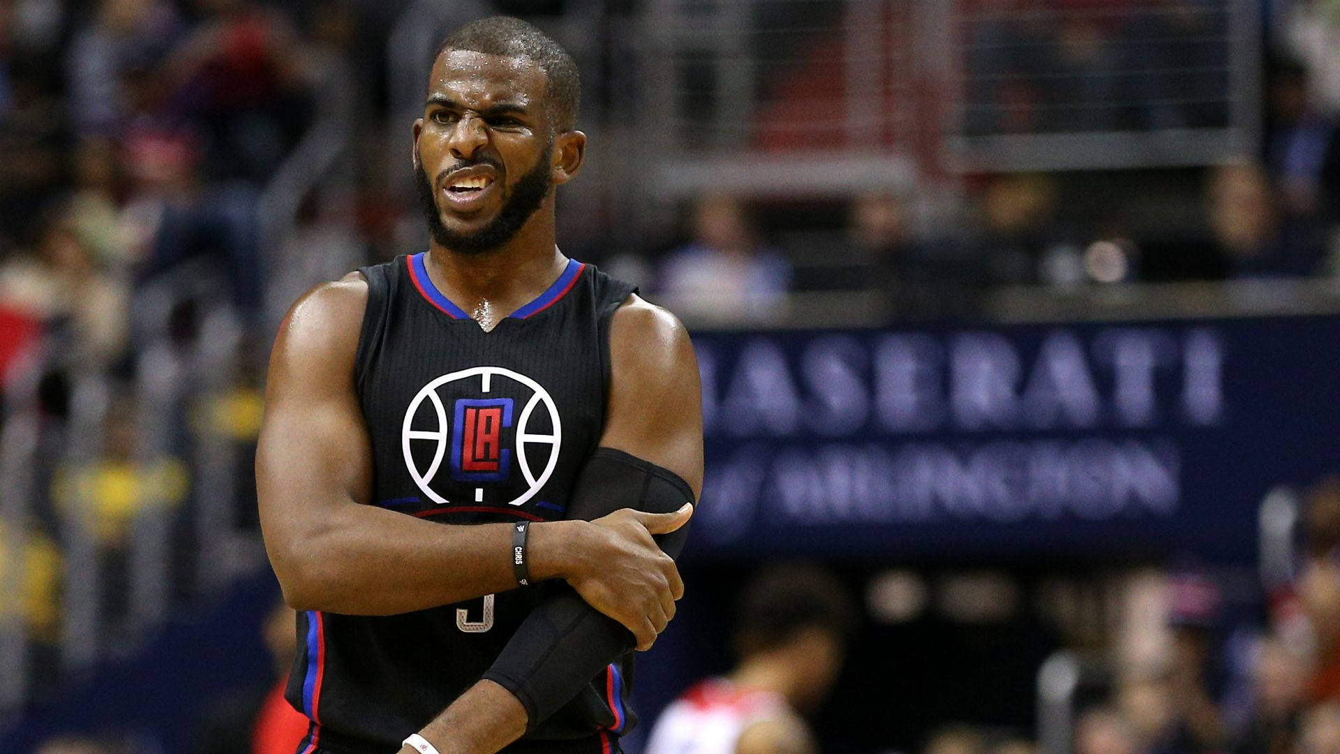 Chris Paul 桌布 壁紙 — 一位專注的籃球運動員身穿黑色洛杉磯快艇隊球衣，在場館燈光下於激烈比賽中交叉雙臂站立。