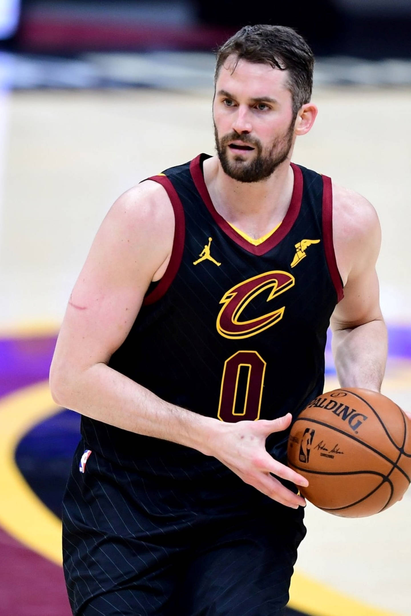 Kevin Love 桌布 壁紙 — 一位專注的籃球運動員身穿黑色騎士隊球衣，在帶有紫色、黃色和藍色標記的球場上運著斯伯丁籃球。