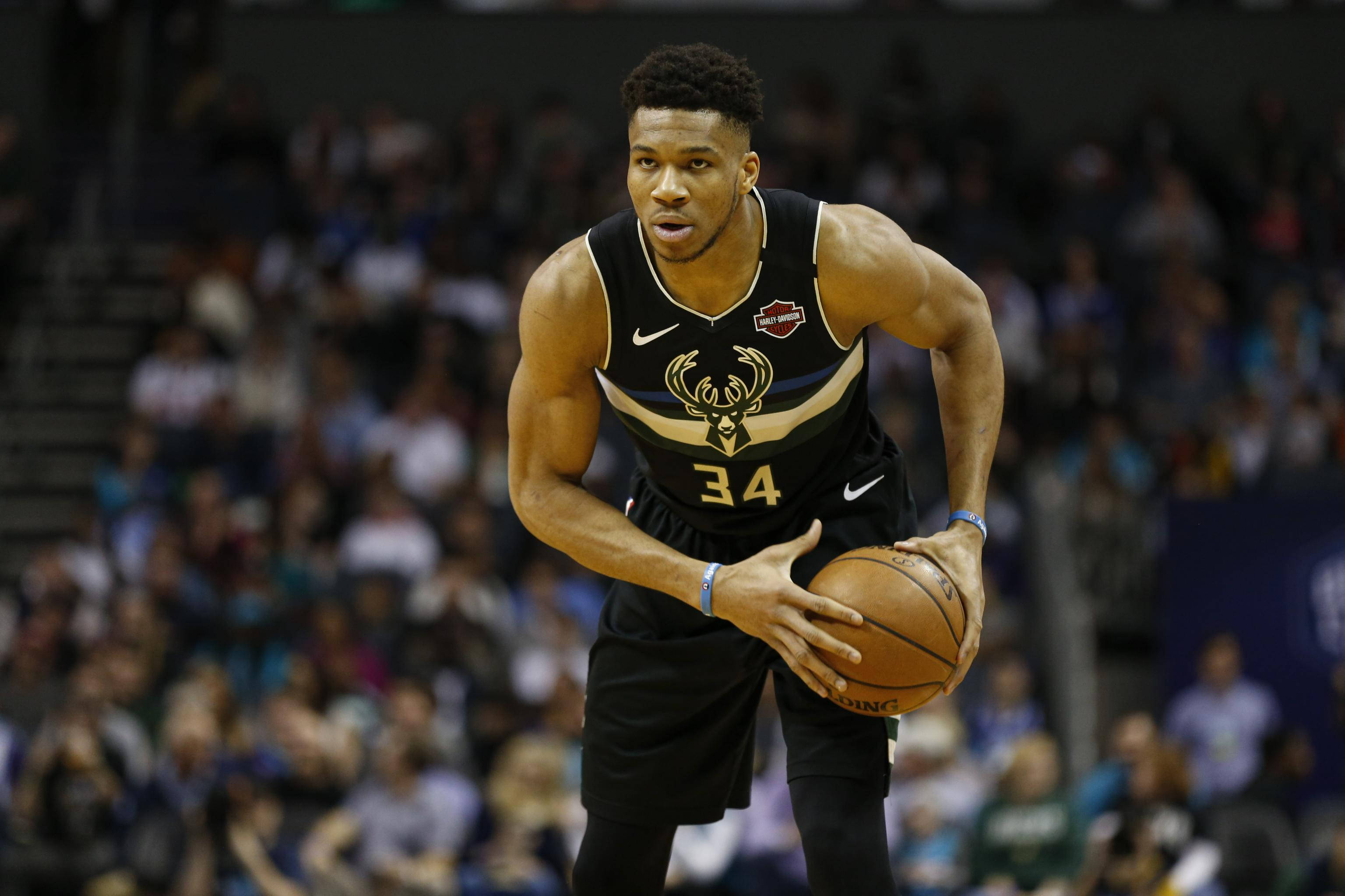 Giannis 桌布 壁紙 — 一位專注的籃球運動員身穿黑金色球衣，在明亮的場館燈光下於激烈的比賽中運球。