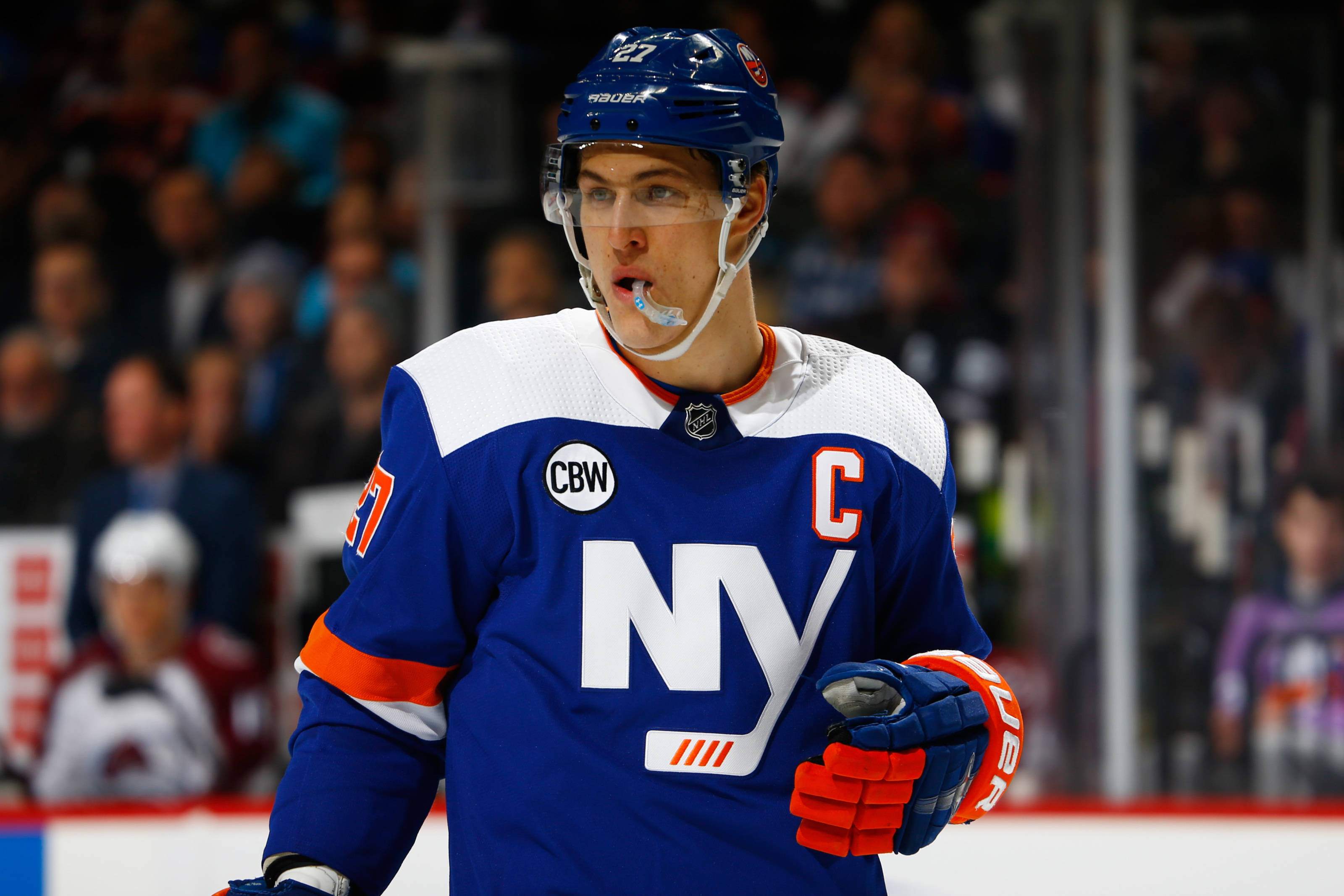 New York Islanders 桌布 壁紙 — 一位專注的紐約島民冰球球員，身穿帶有隊長「C」和橙色點綴的藍色球衣，在比賽期間站在冰上。