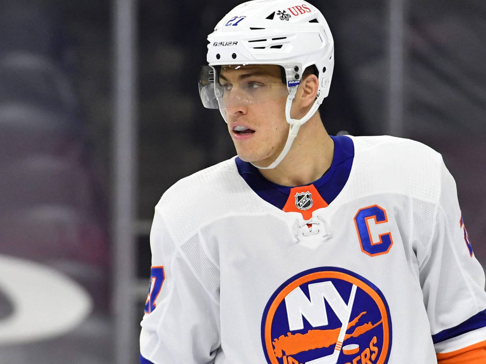 New York Islanders 桌布 壁紙 — 一位專注的紐約島民冰球隊隊長，身穿白色球衣，帶有 'C' 和球隊標誌，在比賽中專注地凝視。