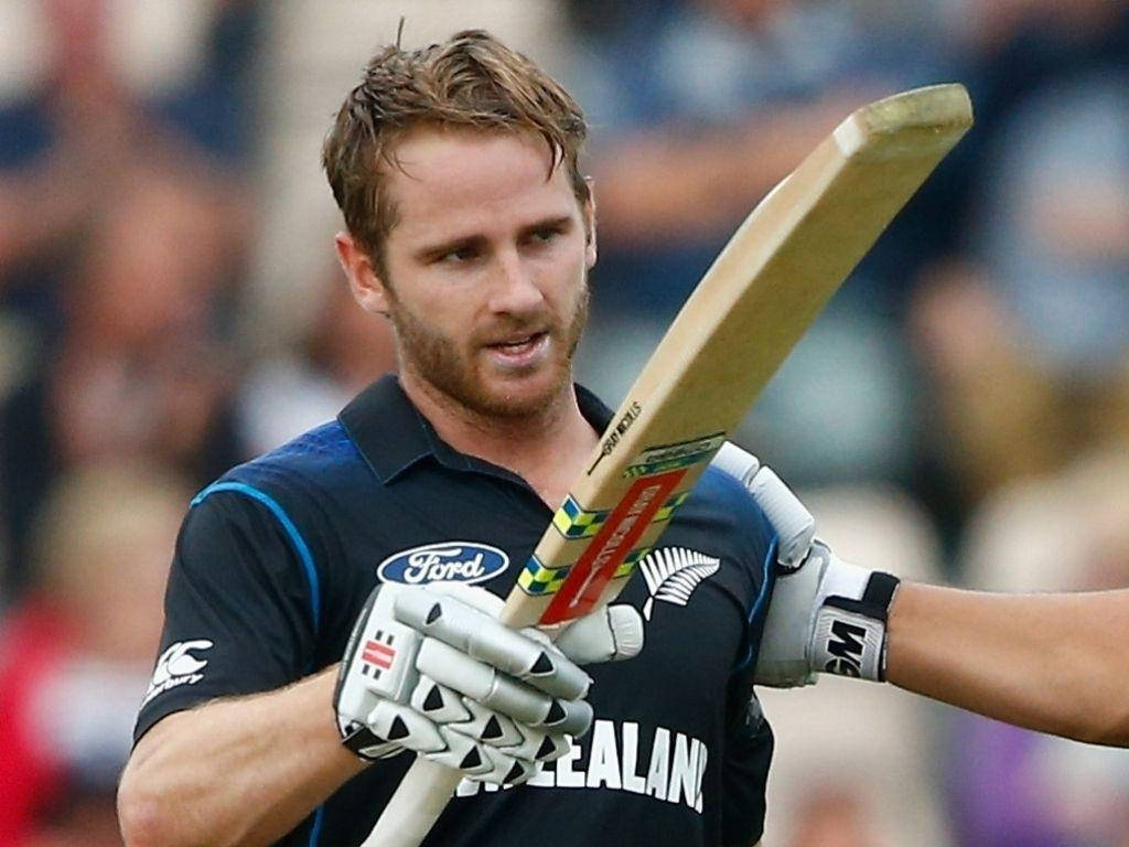 kane williamson 桌布 壁紙 — 一位專注的紐西蘭板球運動員在比賽中緊握球棒，面對模糊的體育場人群，展現出強烈的決心。