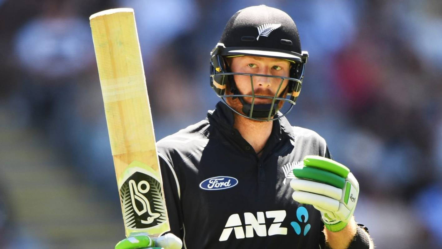 martin guptill 桌布 壁紙 — 一位專注的紐西蘭板球運動員身穿黑色裝備，在明亮的日光下手持木製球棒和綠色手套。
